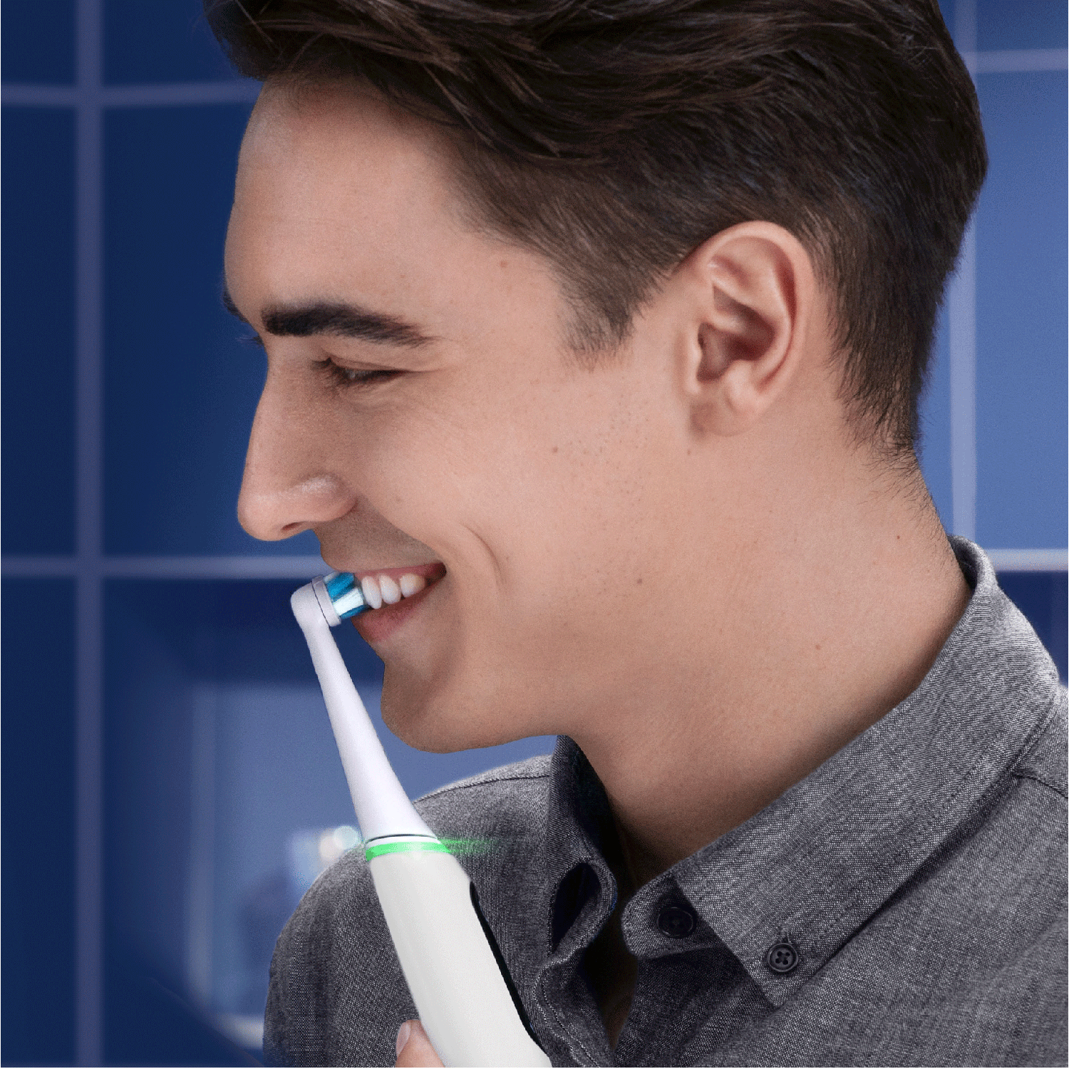Un hombre sonriendo mientras se cepilla los dientes con un cepillo de dientes eléctrico blanco y verde.