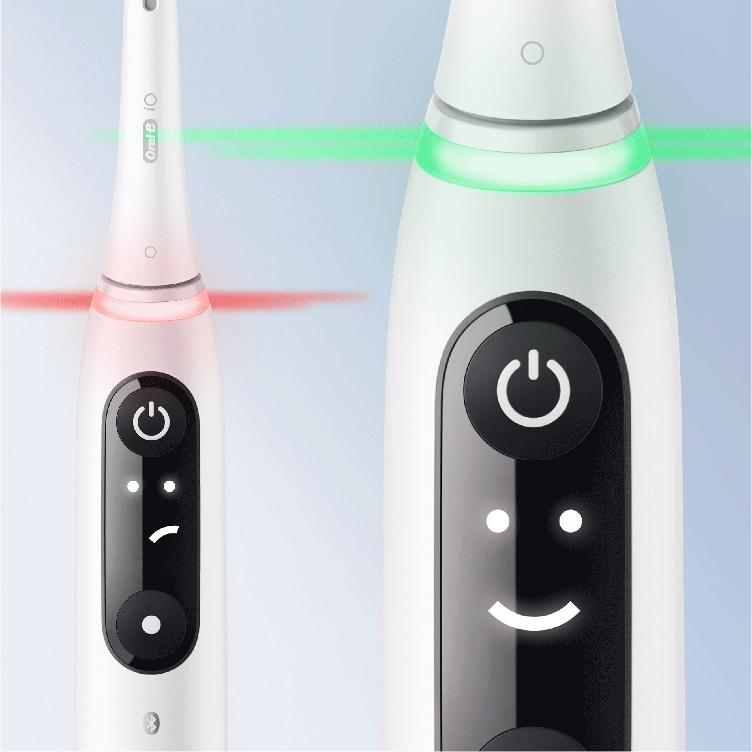 Dos cepillos de dientes eléctricos blancos con botones de encendido iluminados, uno con una carita sonriente.