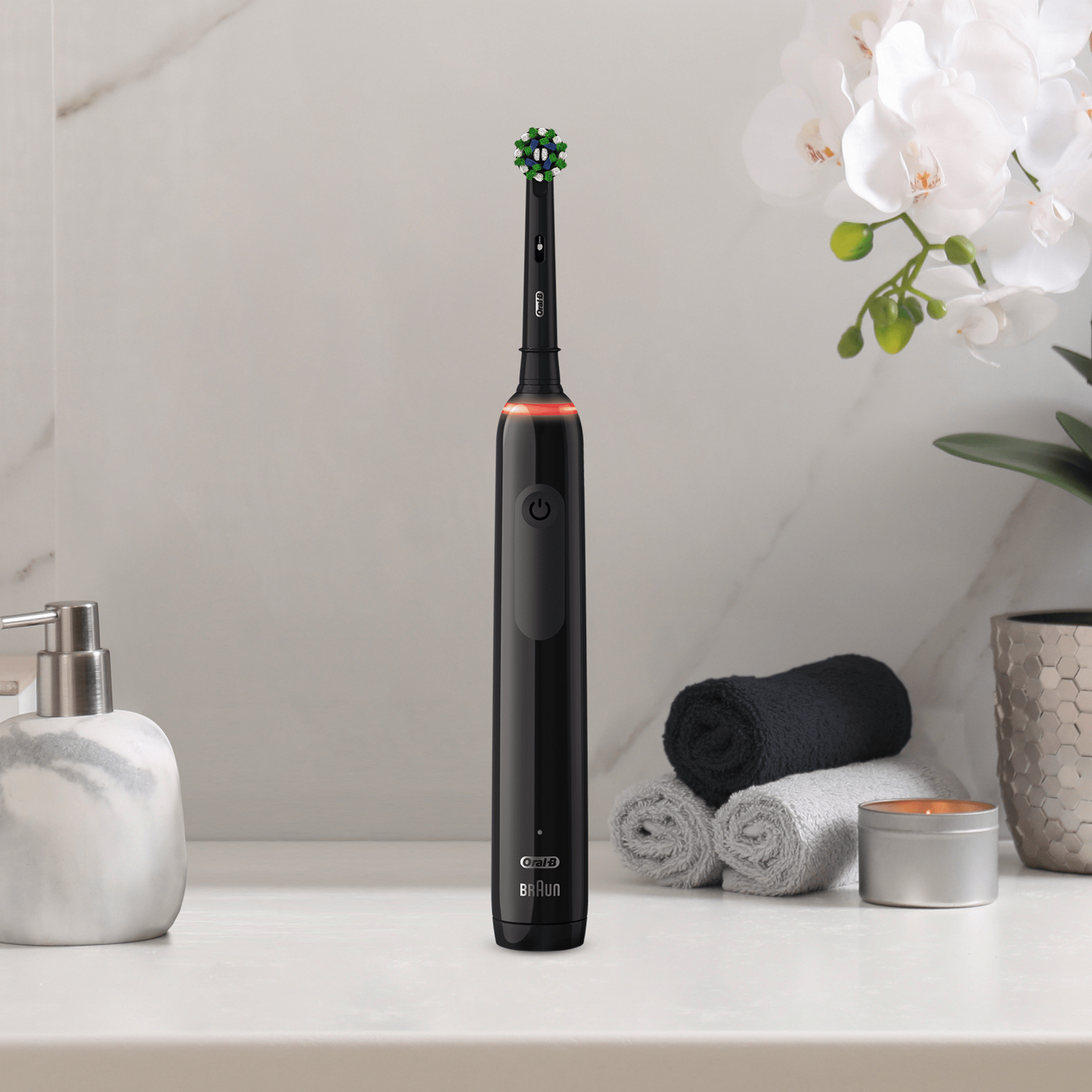 Schwarze elektrische Zahnbürste auf einer Theke. Ein Seifenspender, Handtücher und Blumen sind daneben.