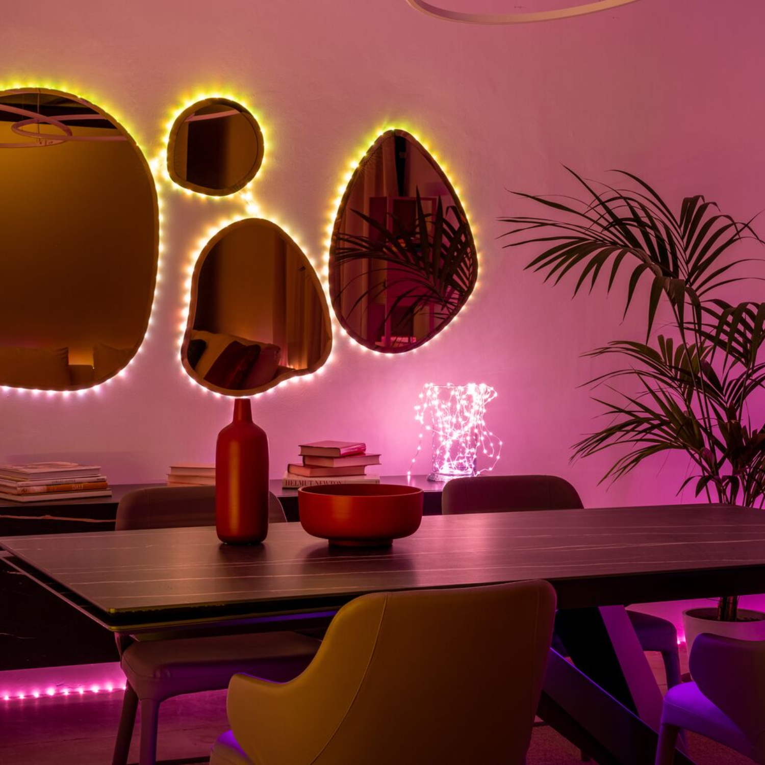 Jadalnia z lustrami, stołem i dekoracyjnym oświetleniem. Obecny jest kwiat i czerwona butelka.