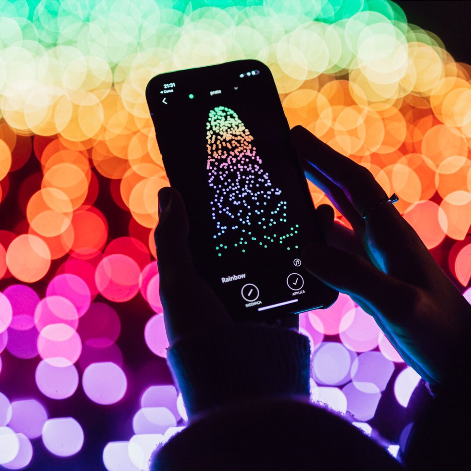 Osoba trzymająca telefon wyświetlający tęczowy wzór świetlny na rozmytym tle.