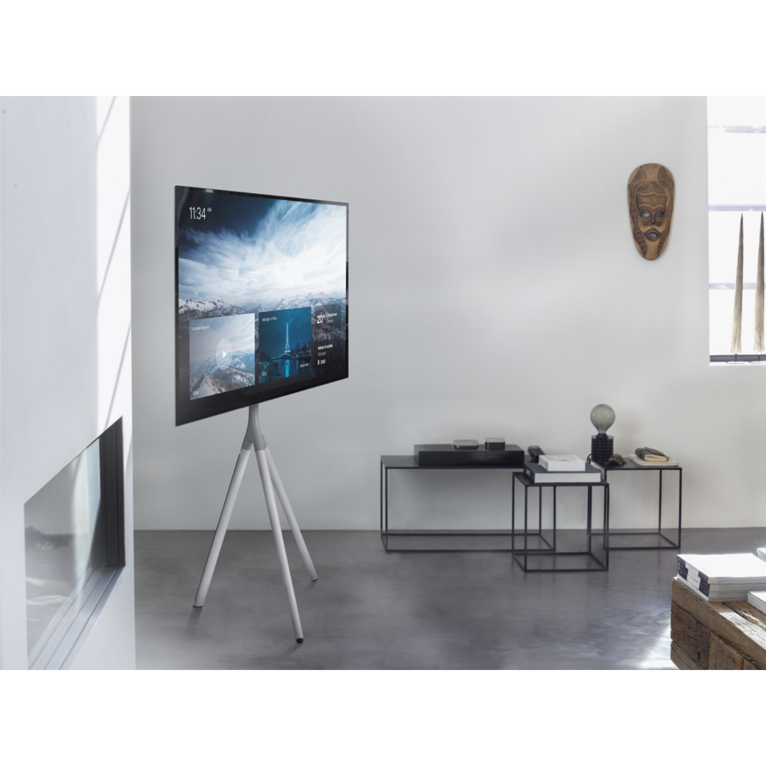 Tv op een wit statief, met een scherm, in een moderne kamer. Er is een masker aan de muur.