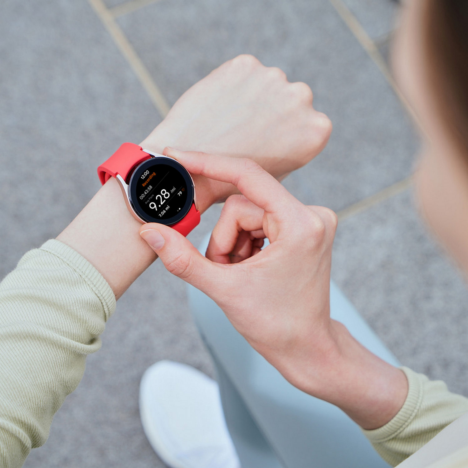 Handgelenk mit Smartwatch, die Zeit und Metriken anzeigt, rotes Band. Hellgrünes Hemd, hellblaue Hose.