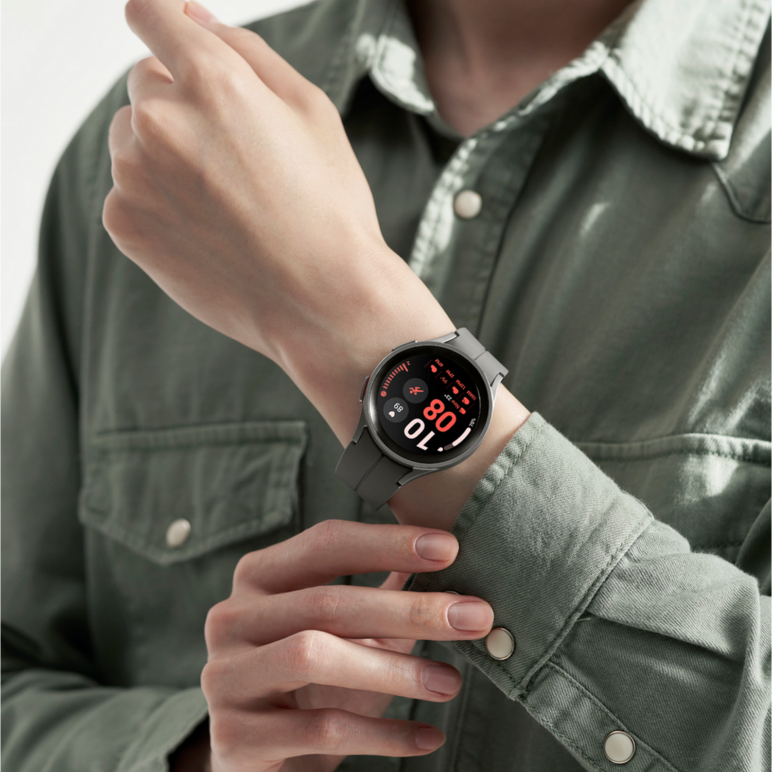 Polso di una persona con smartwatch grigio che mostra ora e statistiche, camicia verde.