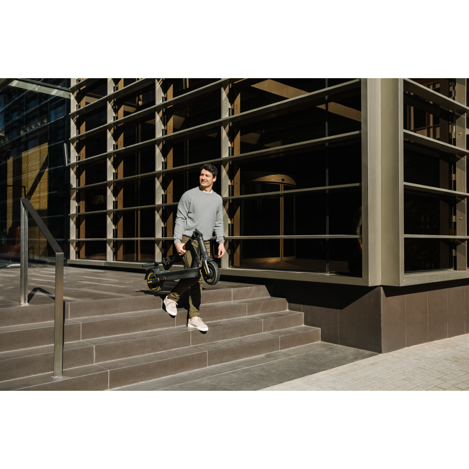 Hombre con patinete baja escaleras frente a edificio.