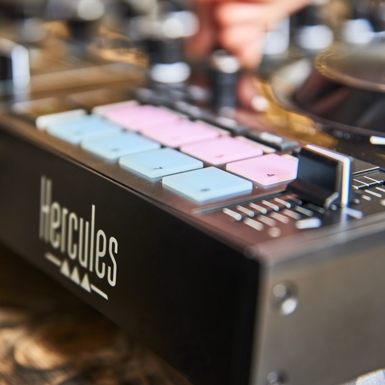 Een Hercules DJ-controller met roze en blauwe knoppen. Een hand past een schuifregelaar aan.