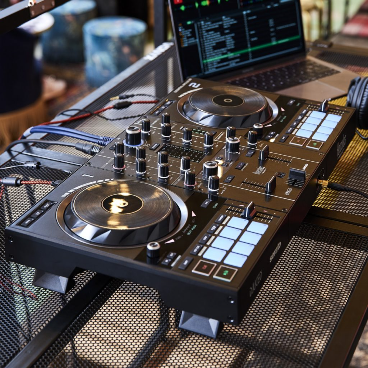 DJ-controller op een zwarte metalen tafel met een laptop, koptelefoon en kabels, bovenaanzicht.