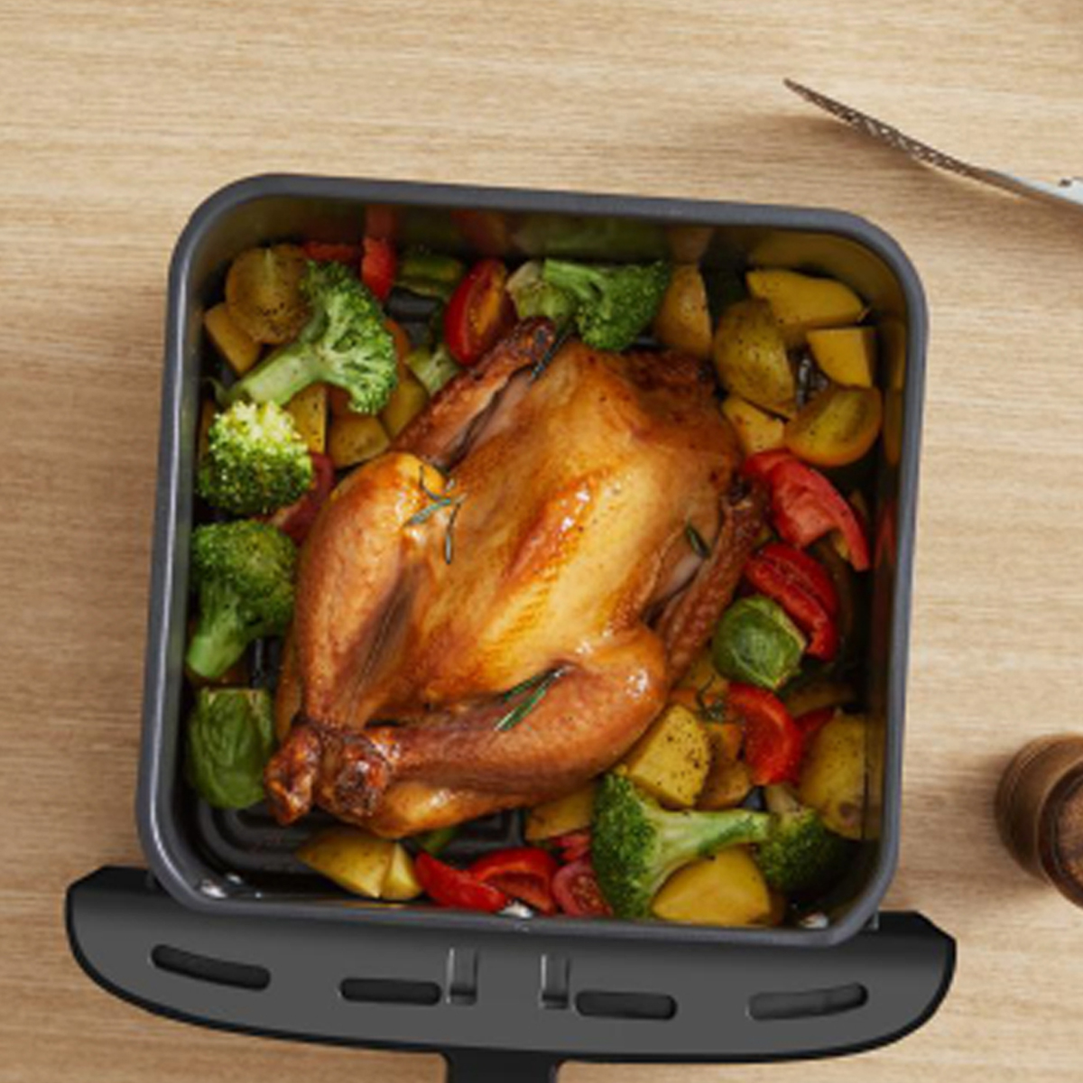 Pollo asado con verduras en una cesta de freidora de aire, colocado sobre una superficie de madera.