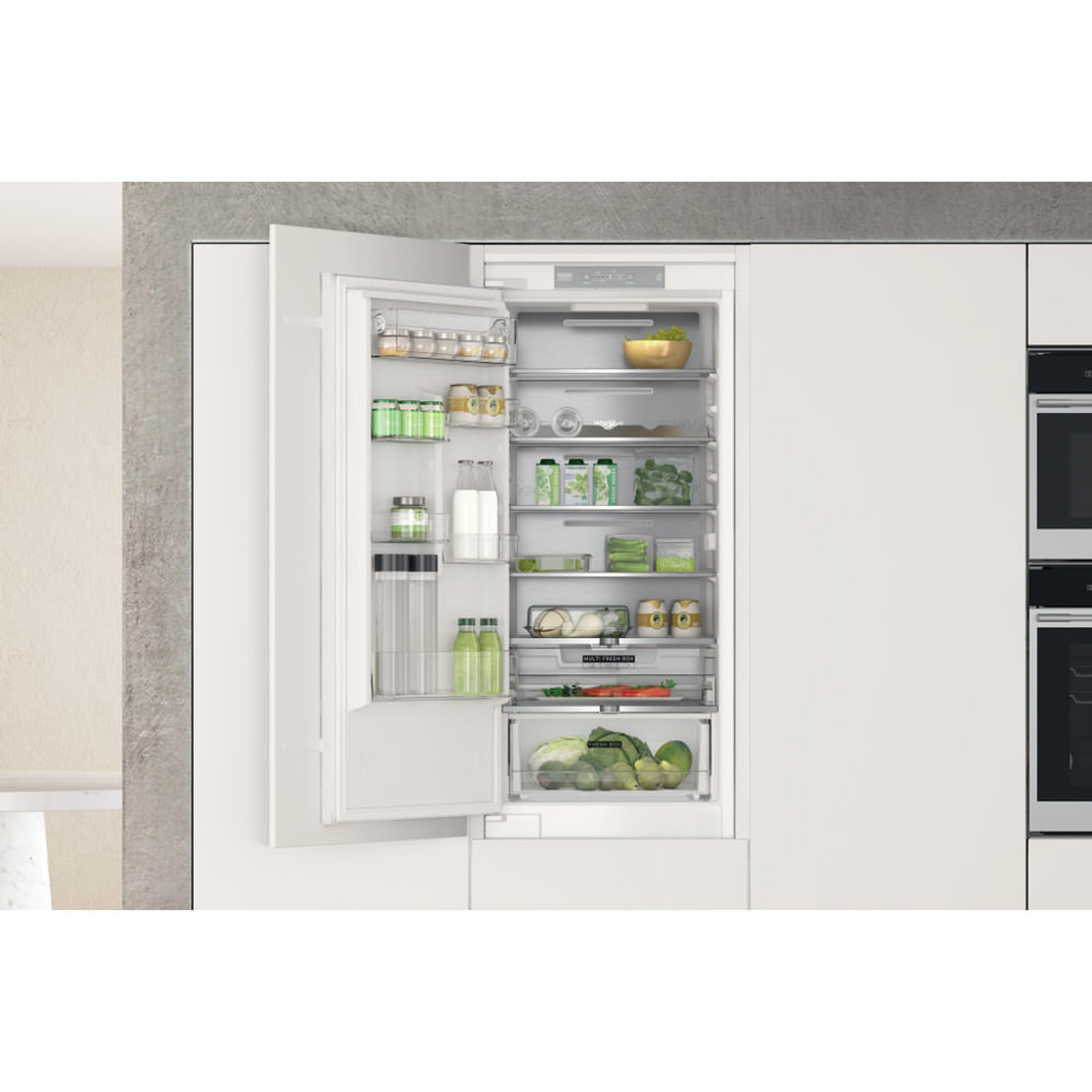 Open inbouwkoelkast met planken vol voedsel, waaronder groenten, fruit en potten.