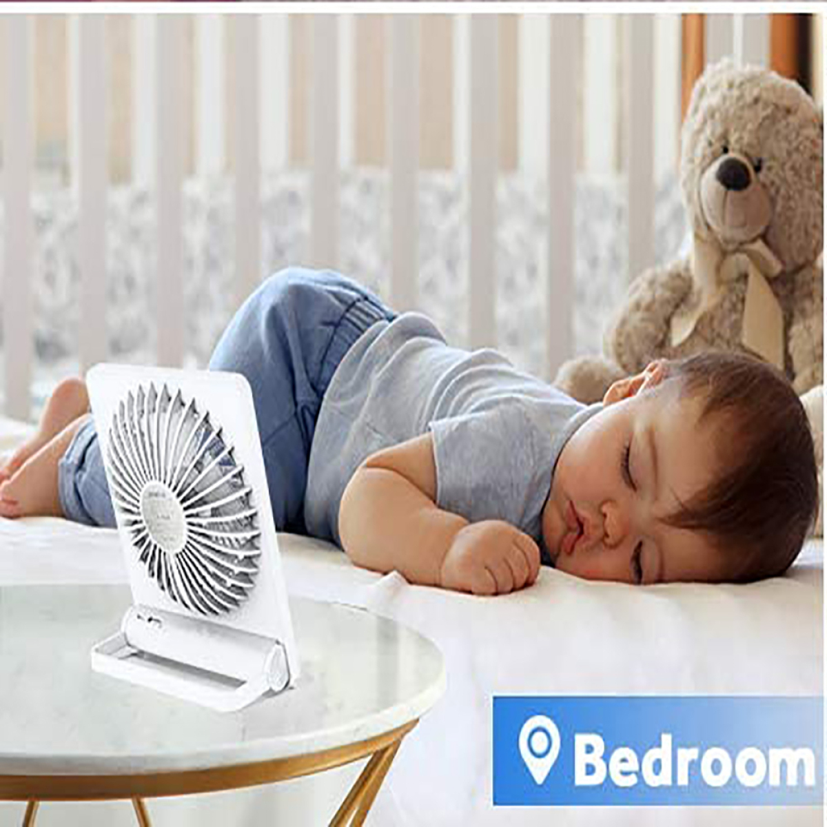 Baby schläft auf einem Bett, ein Ventilator daneben, ein Teddybär in der Nähe.