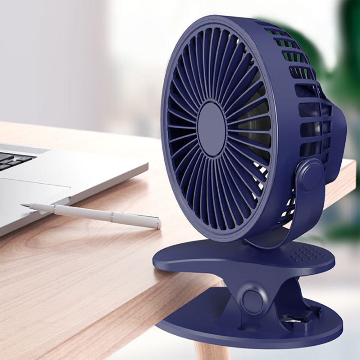 Ein blauer tragbarer Ventilator mit Clip auf einem Holztisch. Ein Stift und Laptop sind sichtbar.