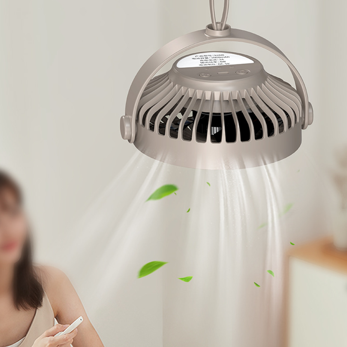 Ein beiger Ventilator mit schwarzen Flügeln hängt von einer weißen Decke. Grüne Blätter schweben in der Luft.