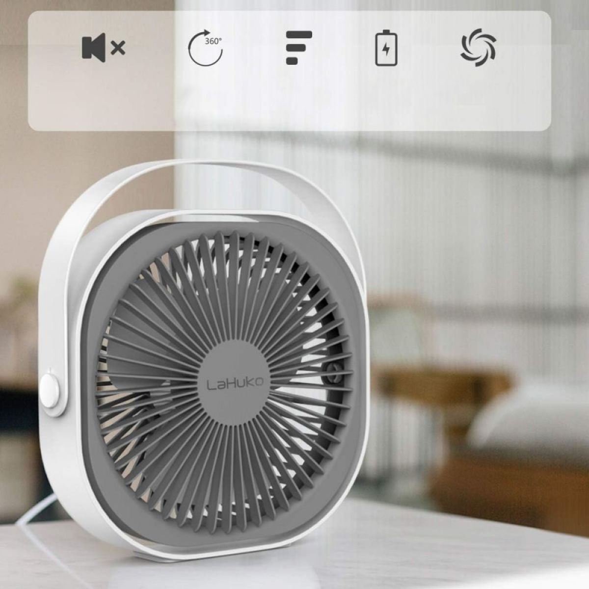 Ein weiß-grauer Ventilator mit Griff auf einem Tisch. Der Ventilator ist eingeschaltet.