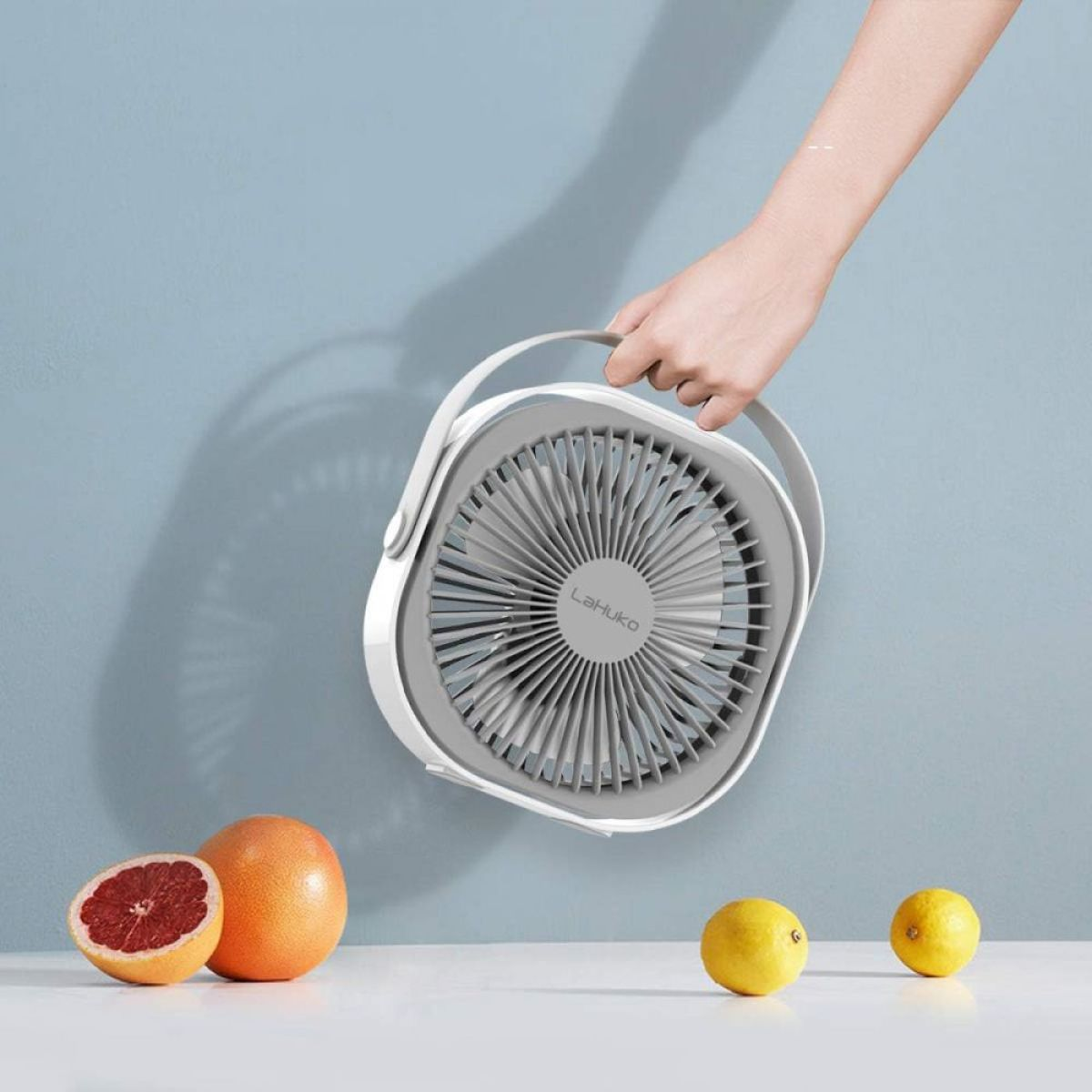 Eine Hand hält einen tragbaren Ventilator, mit Grapefruit und Zitronen.