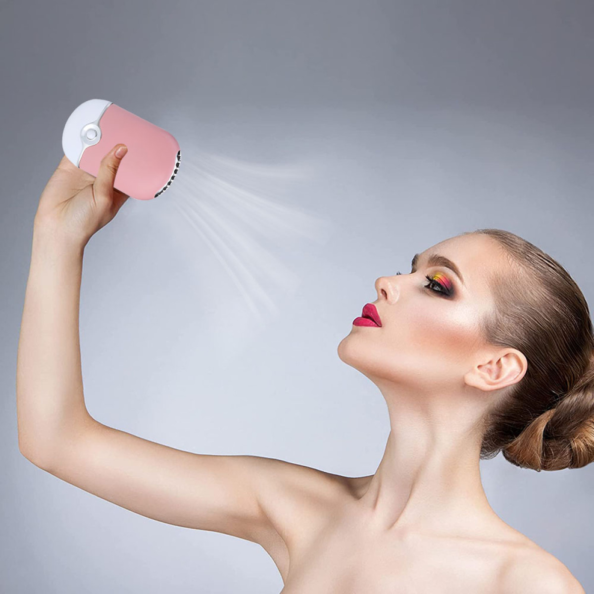 Eine Frau hält einen pinkfarbenen tragbaren Ventilator an ihr Gesicht. Sie hat Make-up und blickt nach oben.