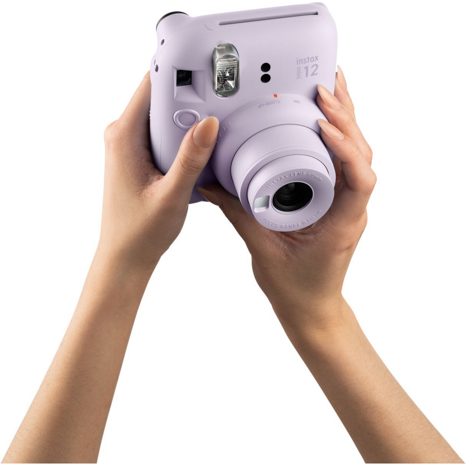 Bir kişi açık mor bir Instax 12 kamera tutuyor. Kamera odaklanmış, eller ön planda.