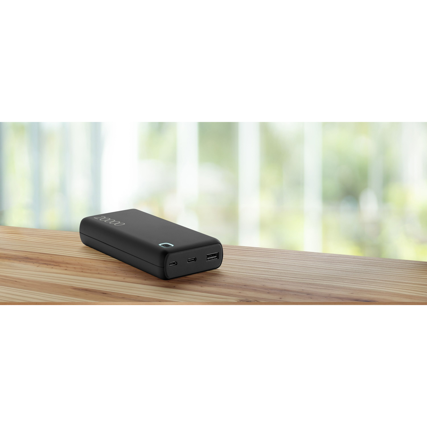 Un power bank nero su un tavolo di legno, con una finestra sfocata sullo sfondo.