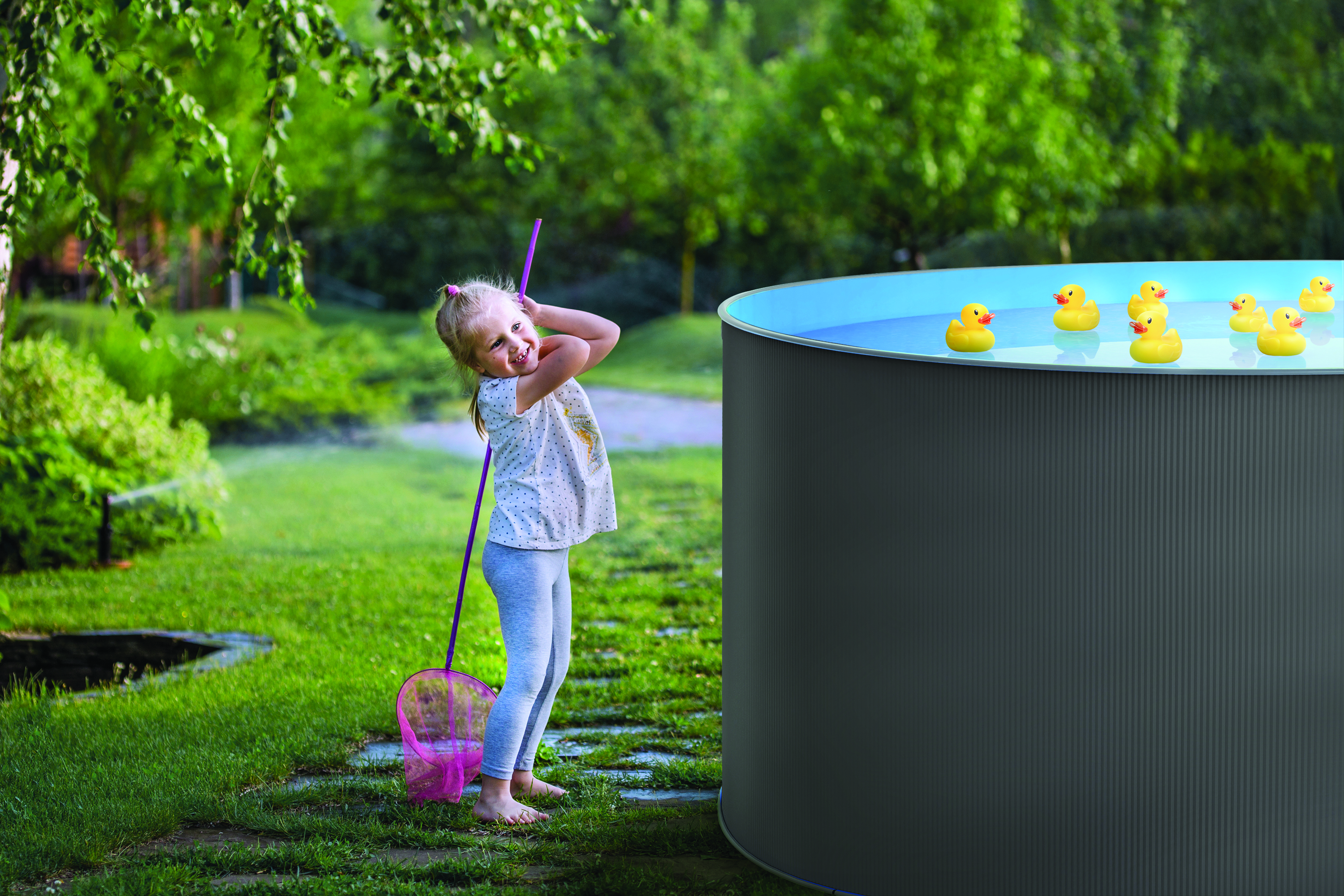 Ein Mädchen mit einem Netz steht an einem Pool mit Gummienten. Es ist ein sonniger Tag im Garten.