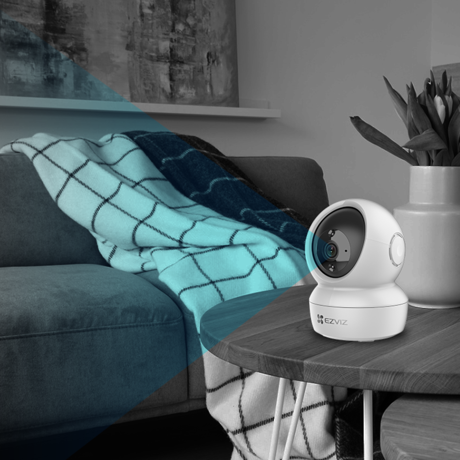 Biała kamera bezpieczeństwa na drewnianym stole. W tle kanapa i koc.