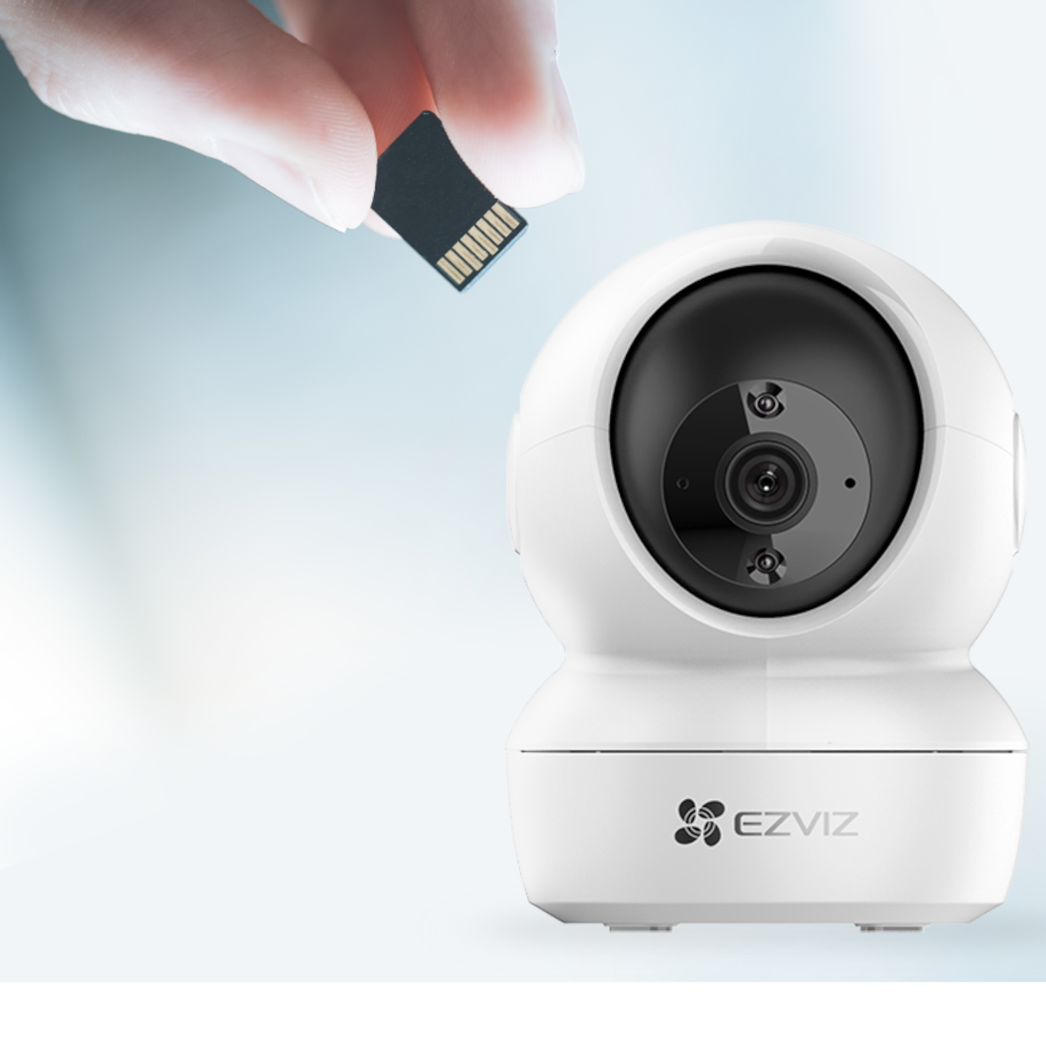 Dłoń trzymająca kartę SD nad białą kamerą bezpieczeństwa.