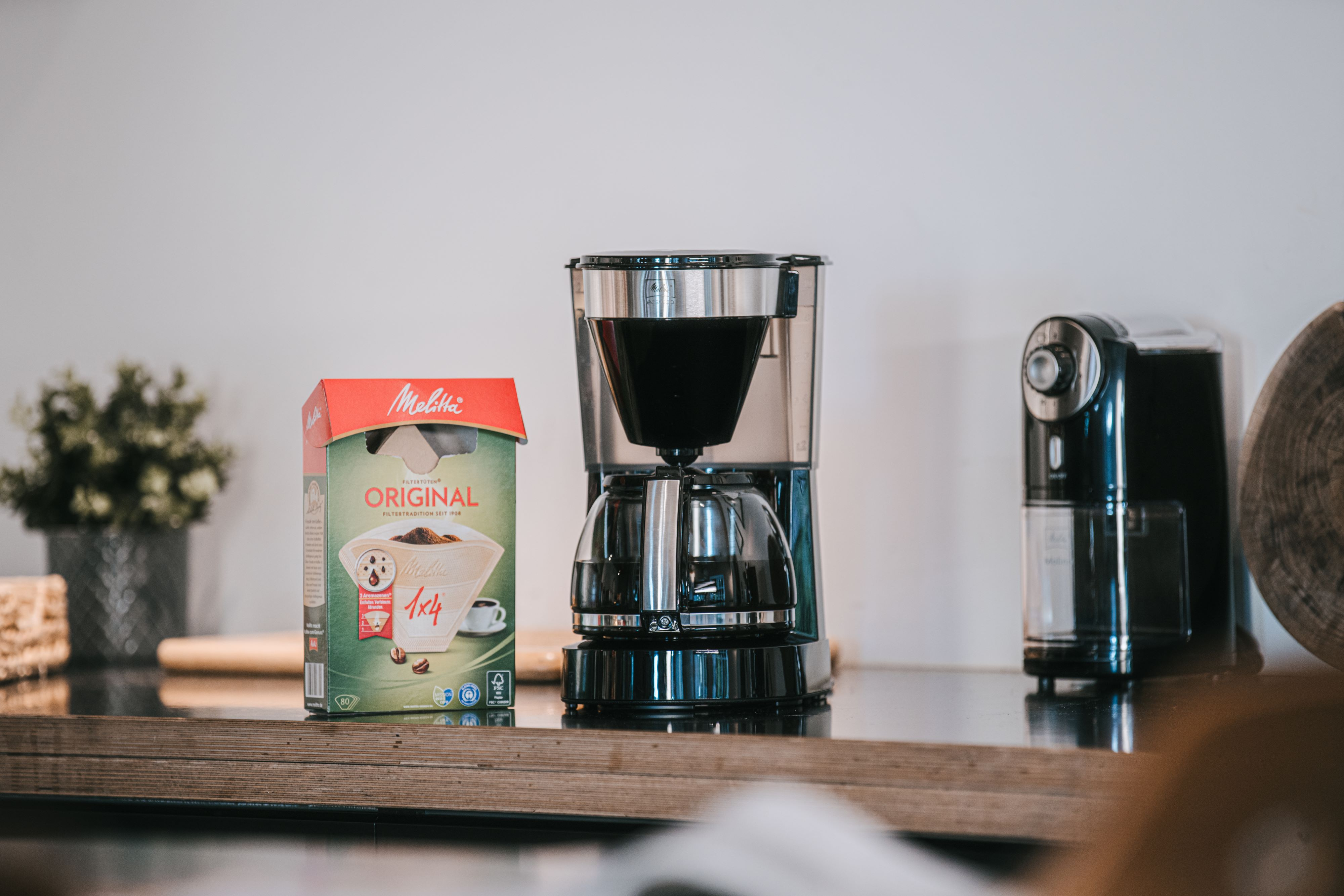 Ekspres do kawy z pudełkiem filtrów do kawy i młynkiem do kawy na drewnianej powierzchni. Tło białej ściany.