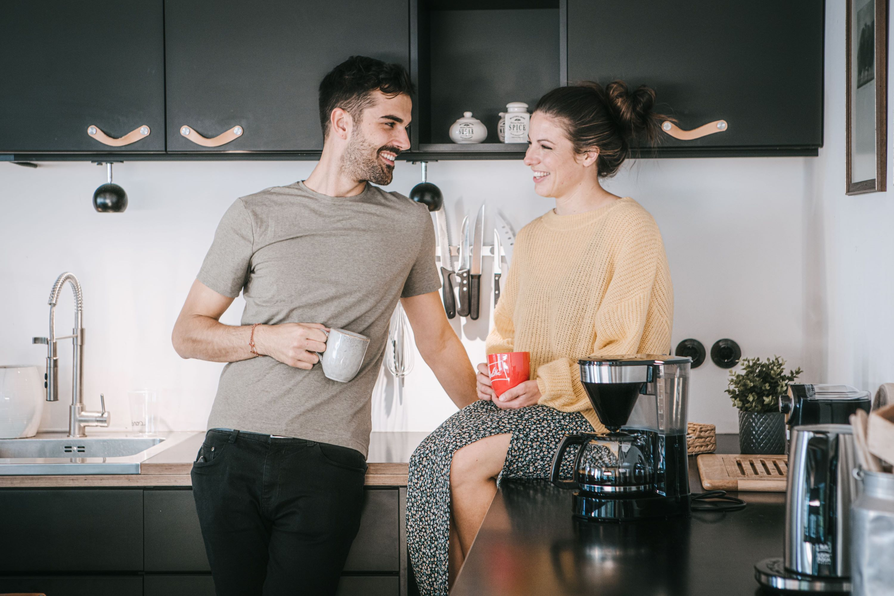 Para w kuchni, uśmiechająca się do siebie. Kobieta opiera się o blat.