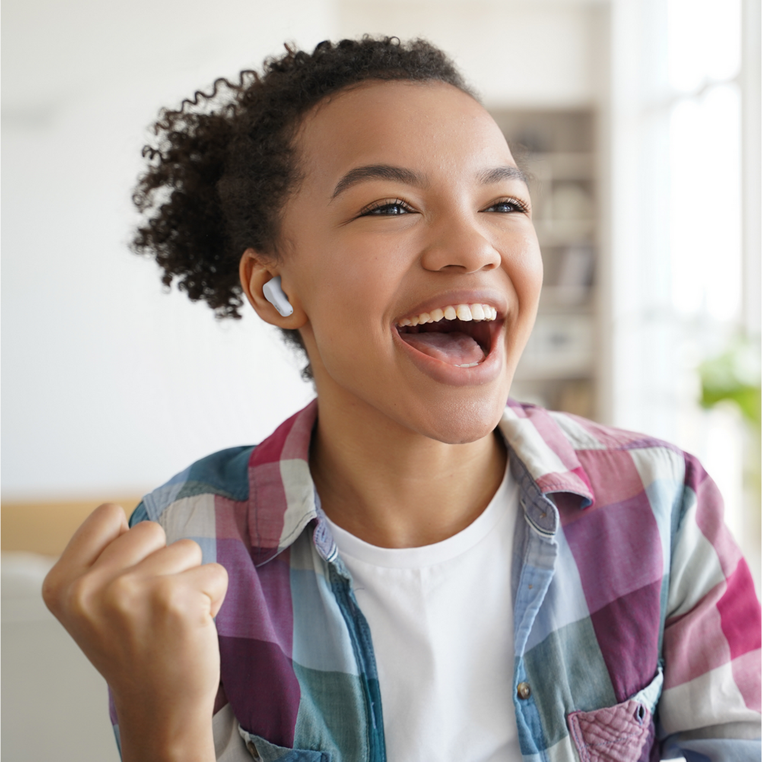 Joven con cabello rizado usando auriculares, sonriendo ampliamente, con el puño en alto.