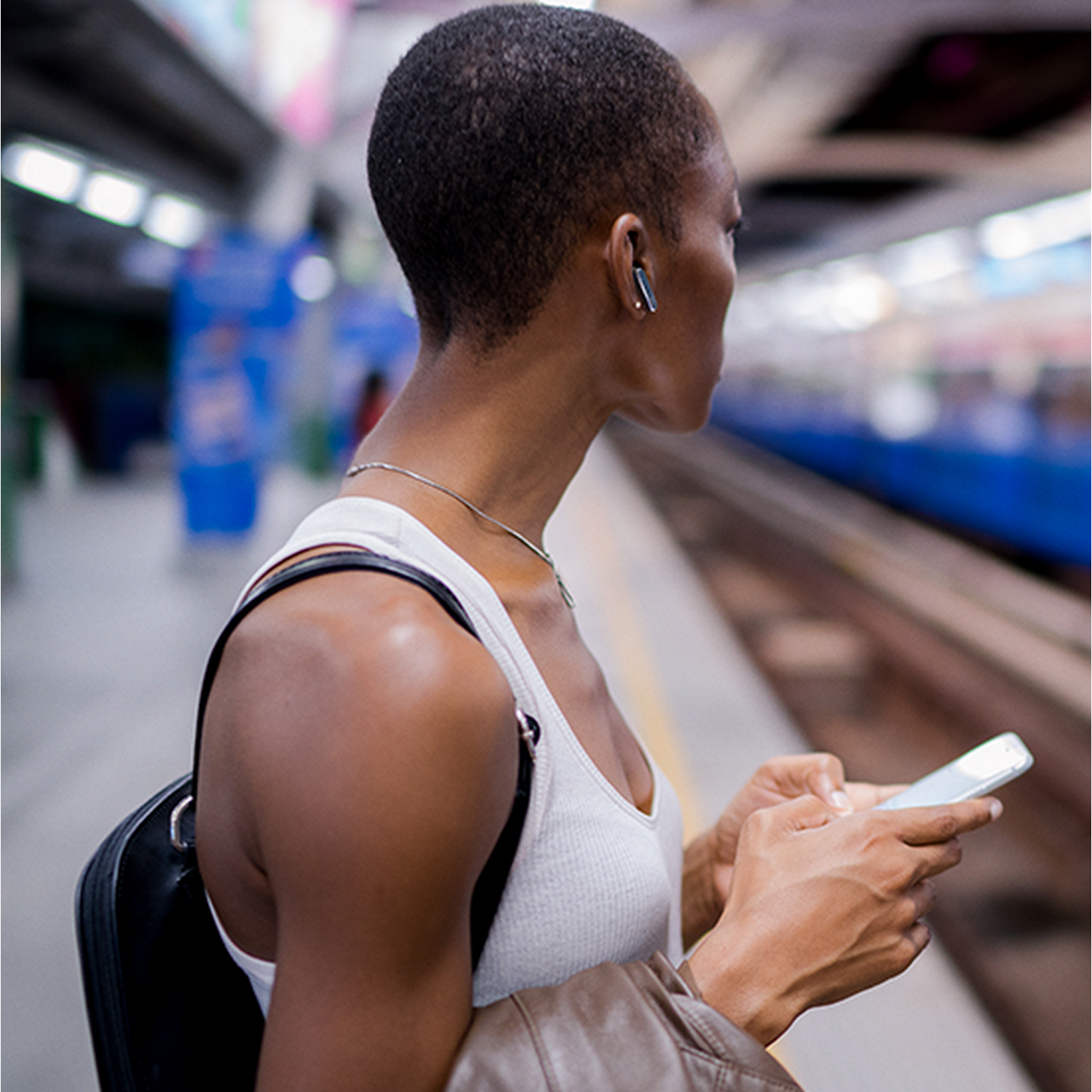 Kobieta na peronie, używająca telefonu, ze słuchawkami, w pobliżu pociągu.