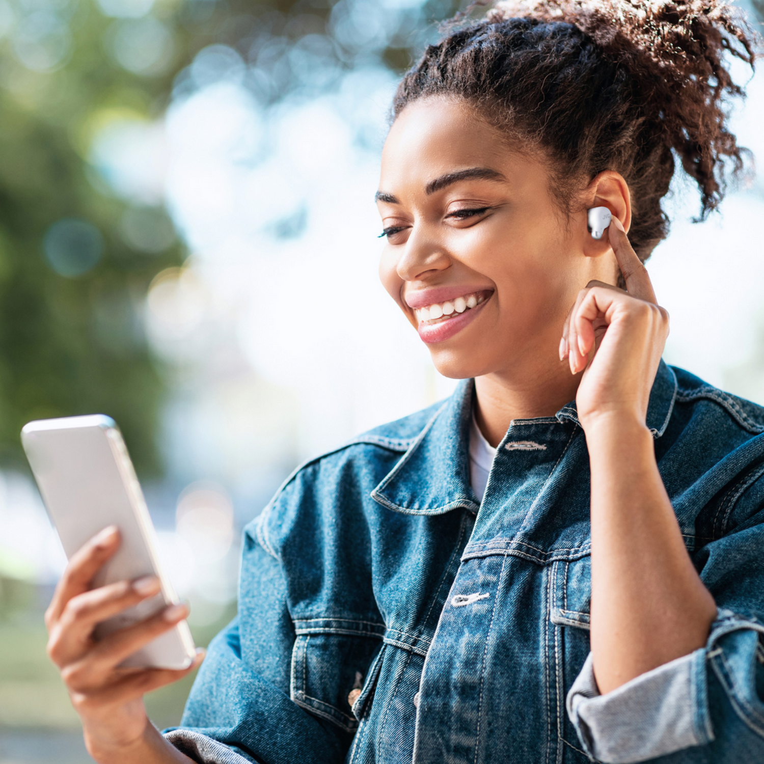 Uśmiechnięta kobieta z telefonem i białymi słuchawkami w uchu.