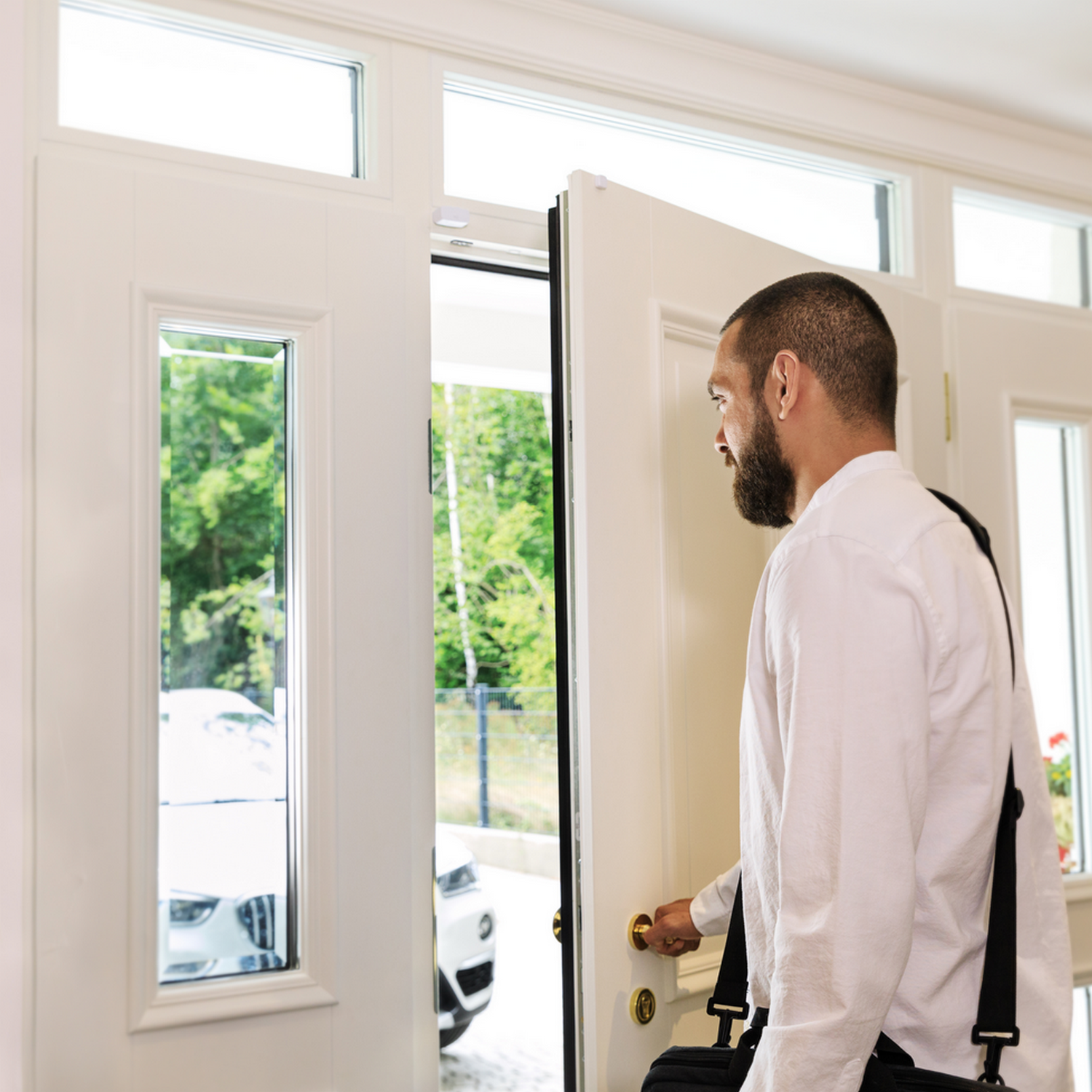 Mężczyzna otwierający białe drzwi do jasnej scenerii na zewnątrz z samochodem.