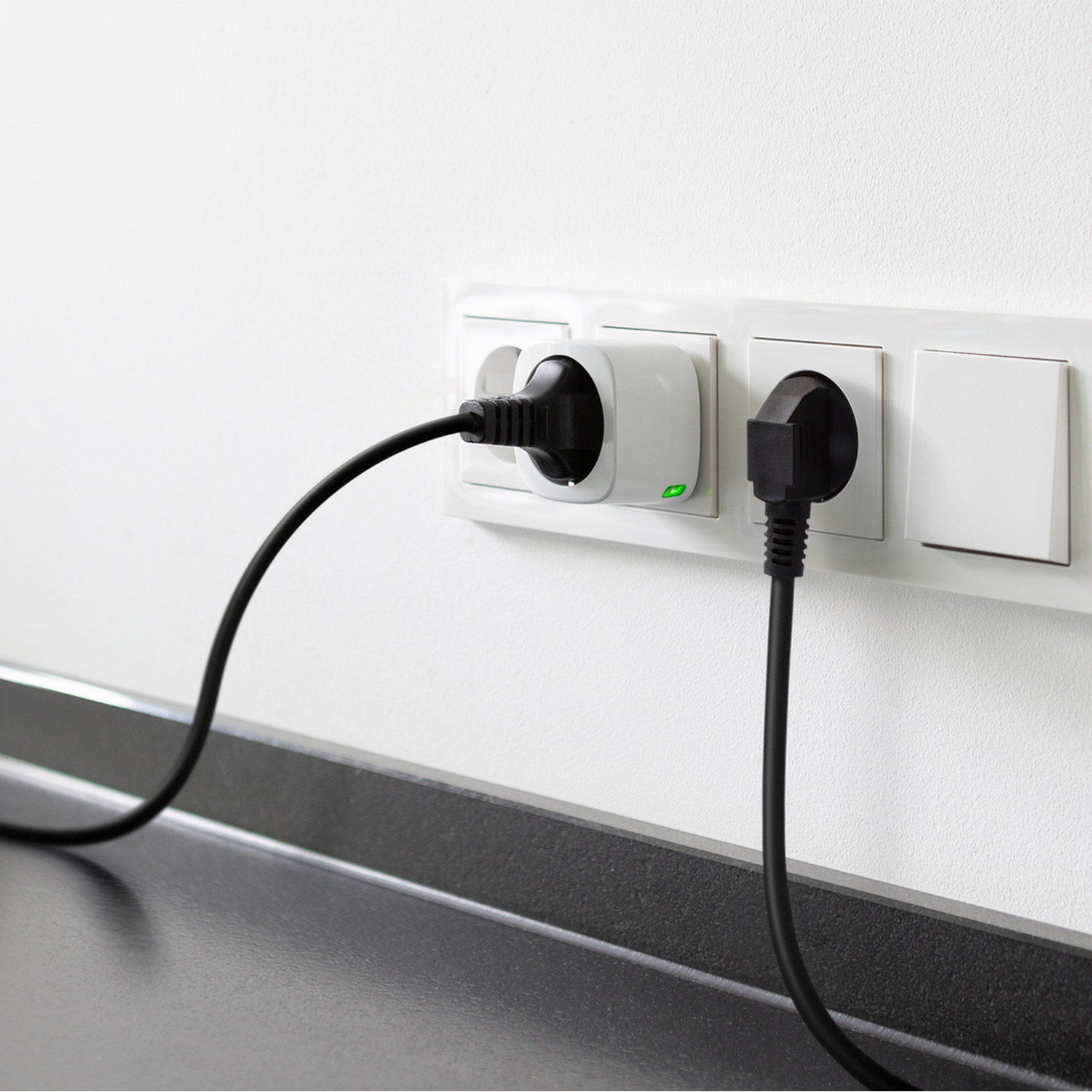 Schwarze Netzstecker stecken in weißen Steckdosen. Schwarze Kabel sind sichtbar. Weiße Wand.
