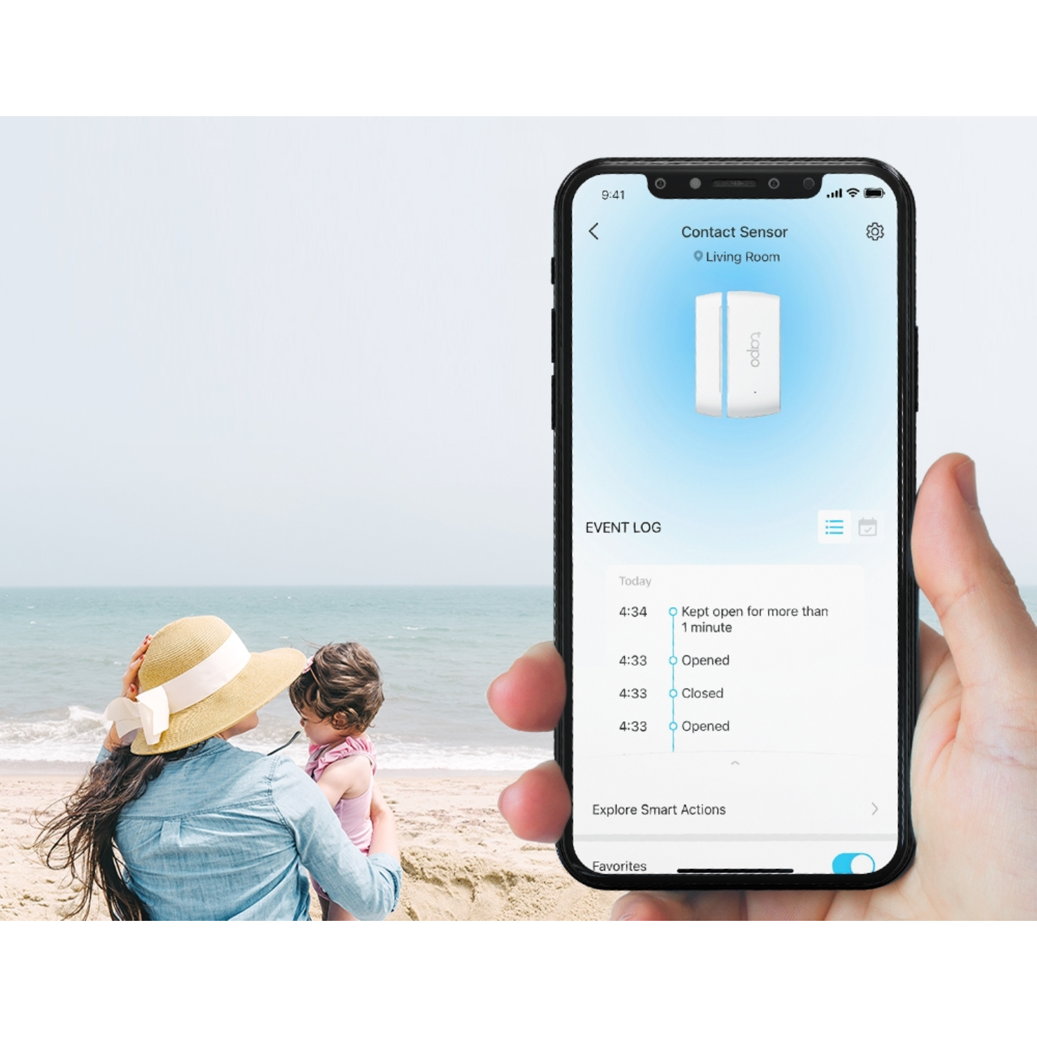 Une personne tenant un téléphone affichant une application domotique, avec une plage et une femme avec un enfant en arrière-plan.