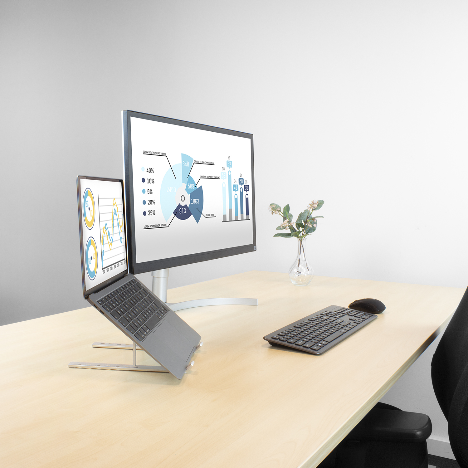 Bürotisch mit Monitor, der Diagramme anzeigt, Laptop, Tastatur, Maus und Vase mit Blumen.