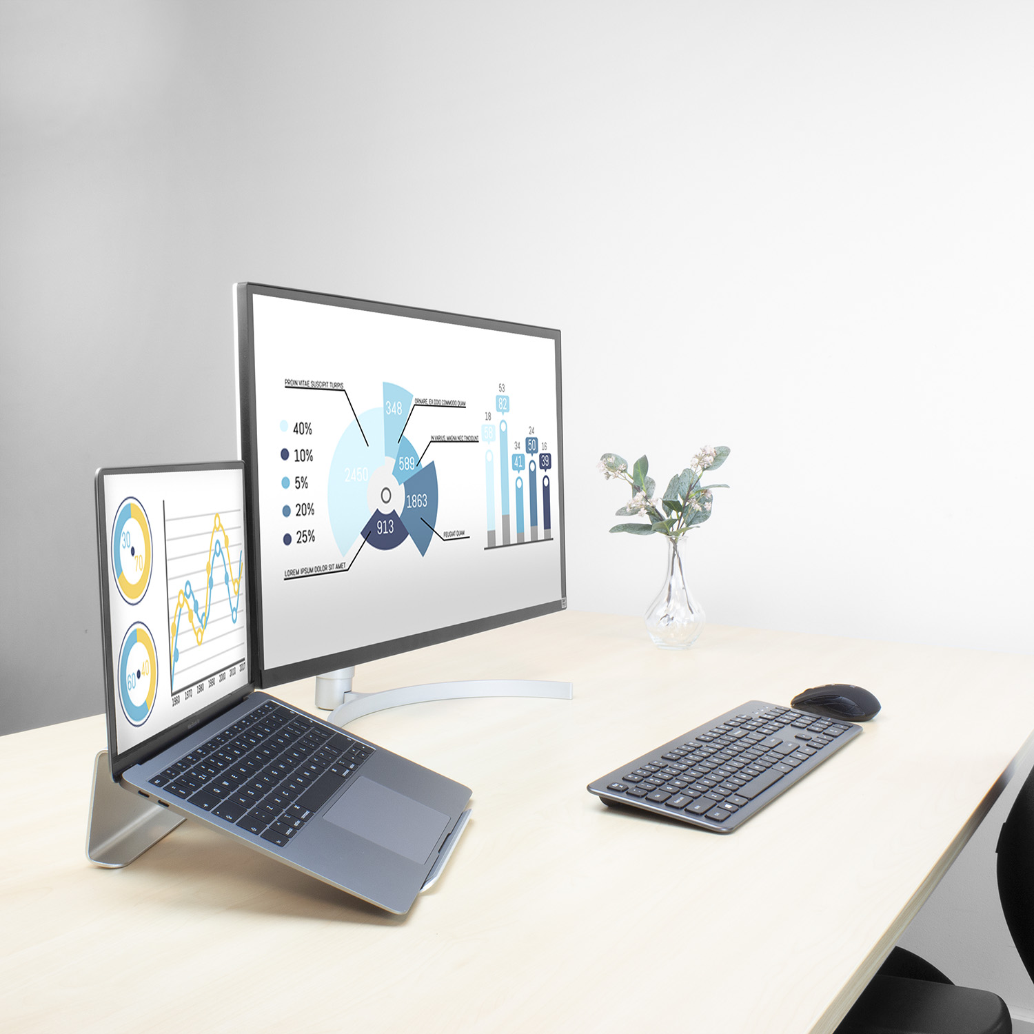 Schreibtisch mit Laptop und Monitor, die Diagramme anzeigen. Maus, Tastatur und eine Vase sind ebenfalls sichtbar.