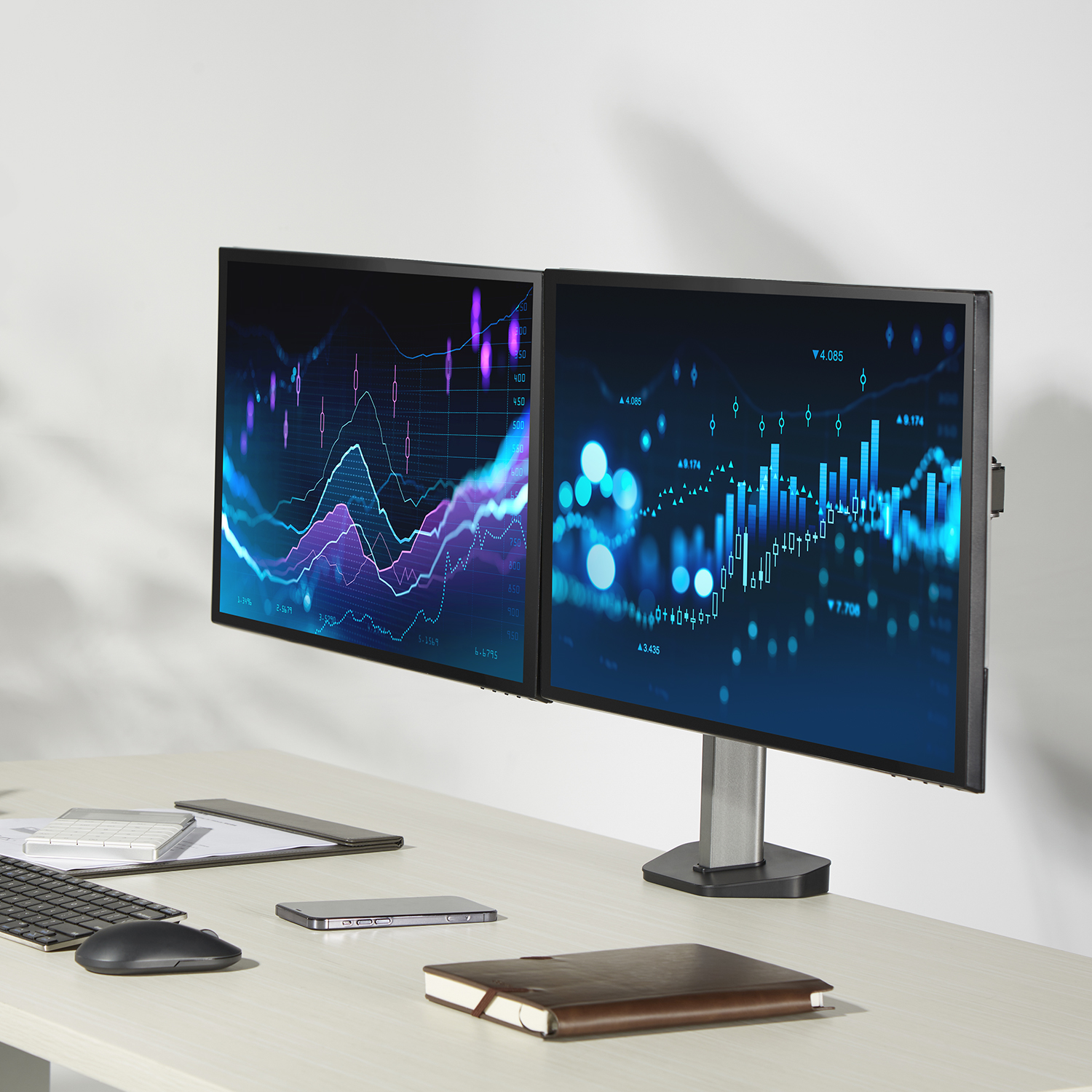 Zwei Computermonitore auf einem Ständer, die Datengraphen anzeigen, auf einem hellen Holzschreibtisch.