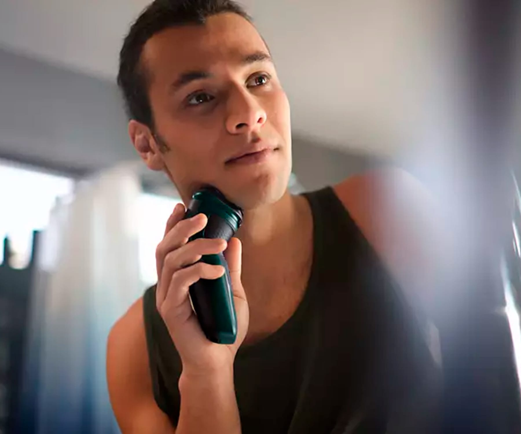 Mężczyzna goli twarz golarką elektryczną, w łazience.