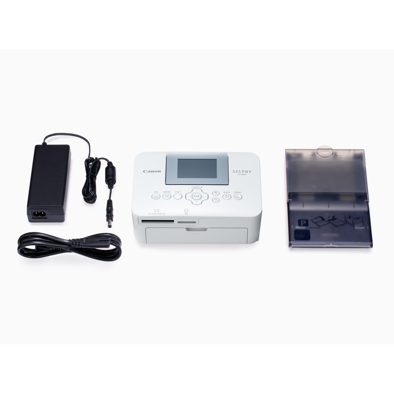 Biała drukarka Canon Selphy z akcesoriami: zasilacz, kabel ładujący i taca na zdjęcia.