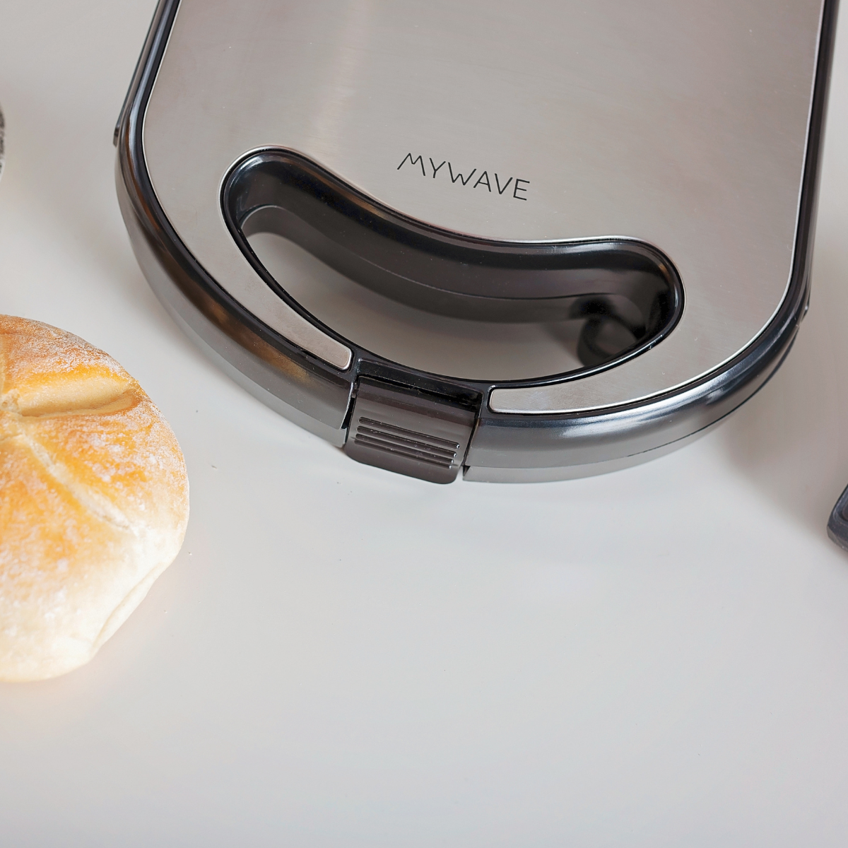 Una sandwichera de acero inoxidable con la palabra "MYWAVE". Un pan está a la izquierda.
