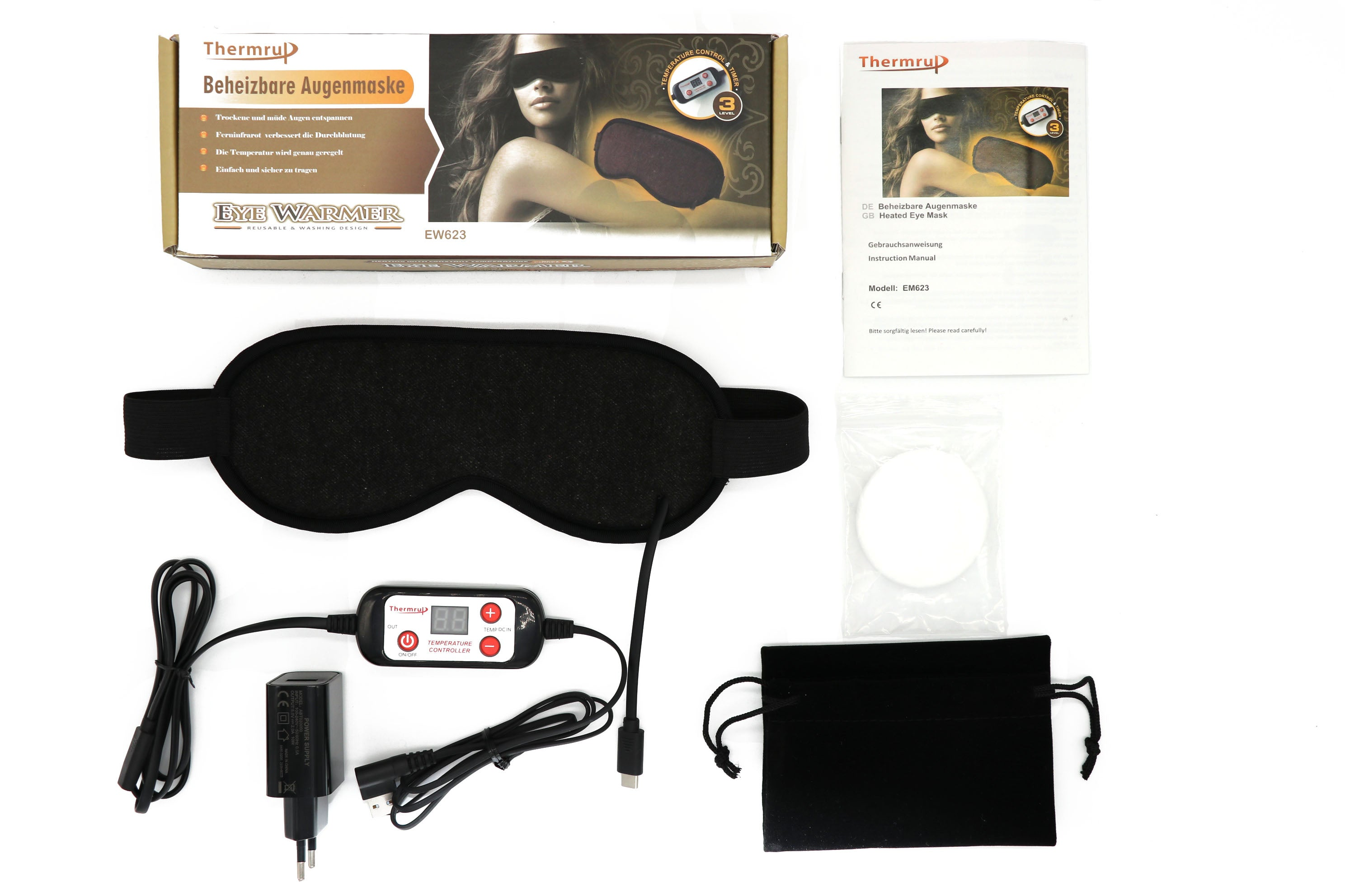 Beheizte Augenmaske mit Schachtel, Kabel, Adapter und Zubehör, alles auf weißer Oberfläche. Die Schachtel hat ein Frauenbild.