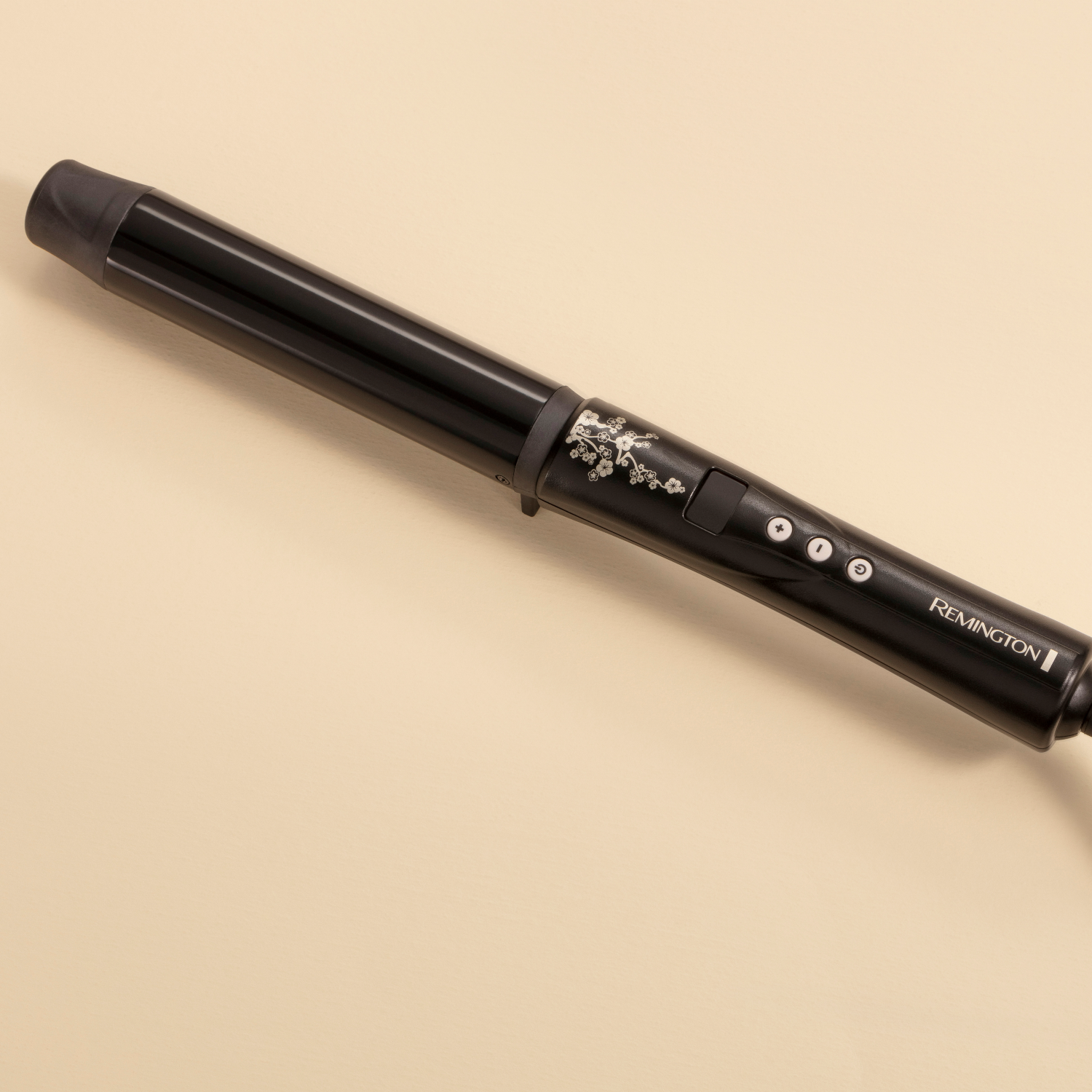 Fer à friser Remington noir sur une surface beige, légèrement incliné vers la droite.