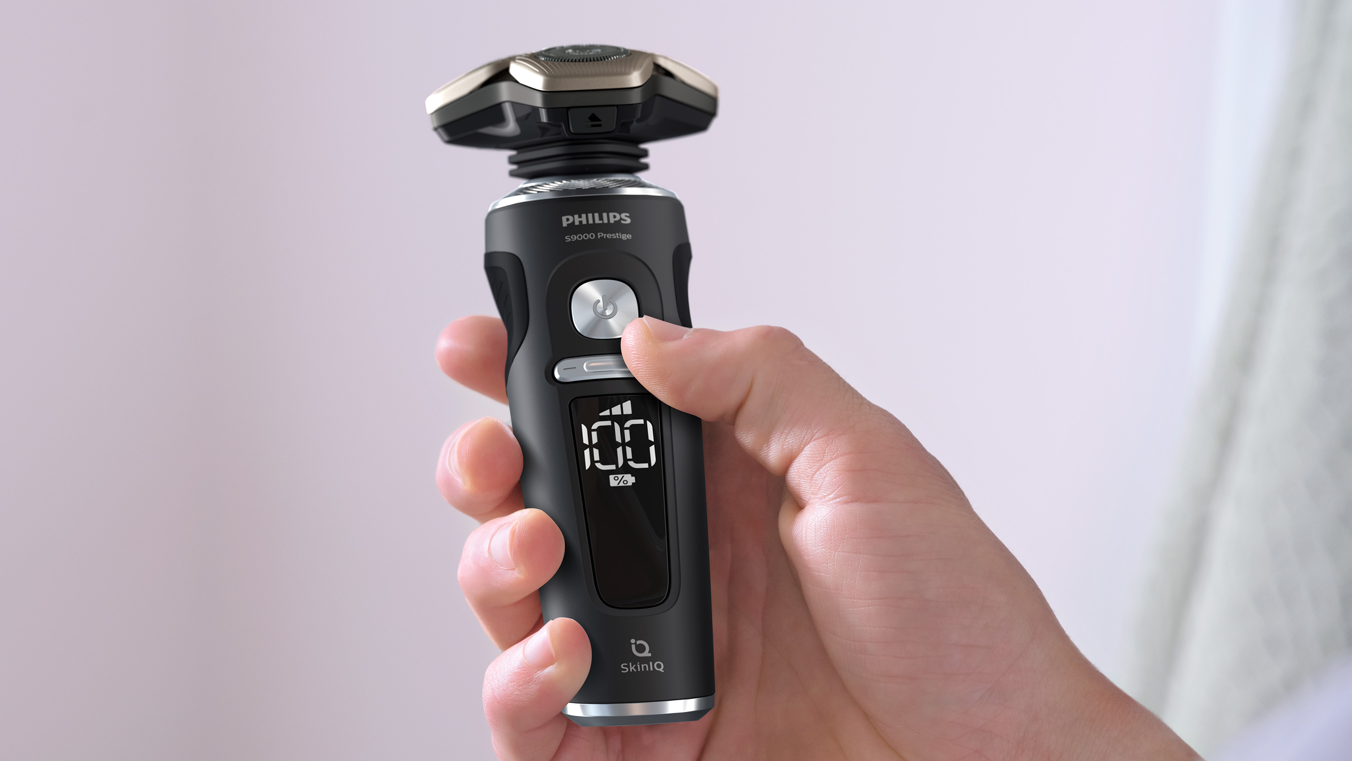 Hand hält schwarzen Philips Rasierer, Display zeigt 100%. Hintergrund ist verschwommen.