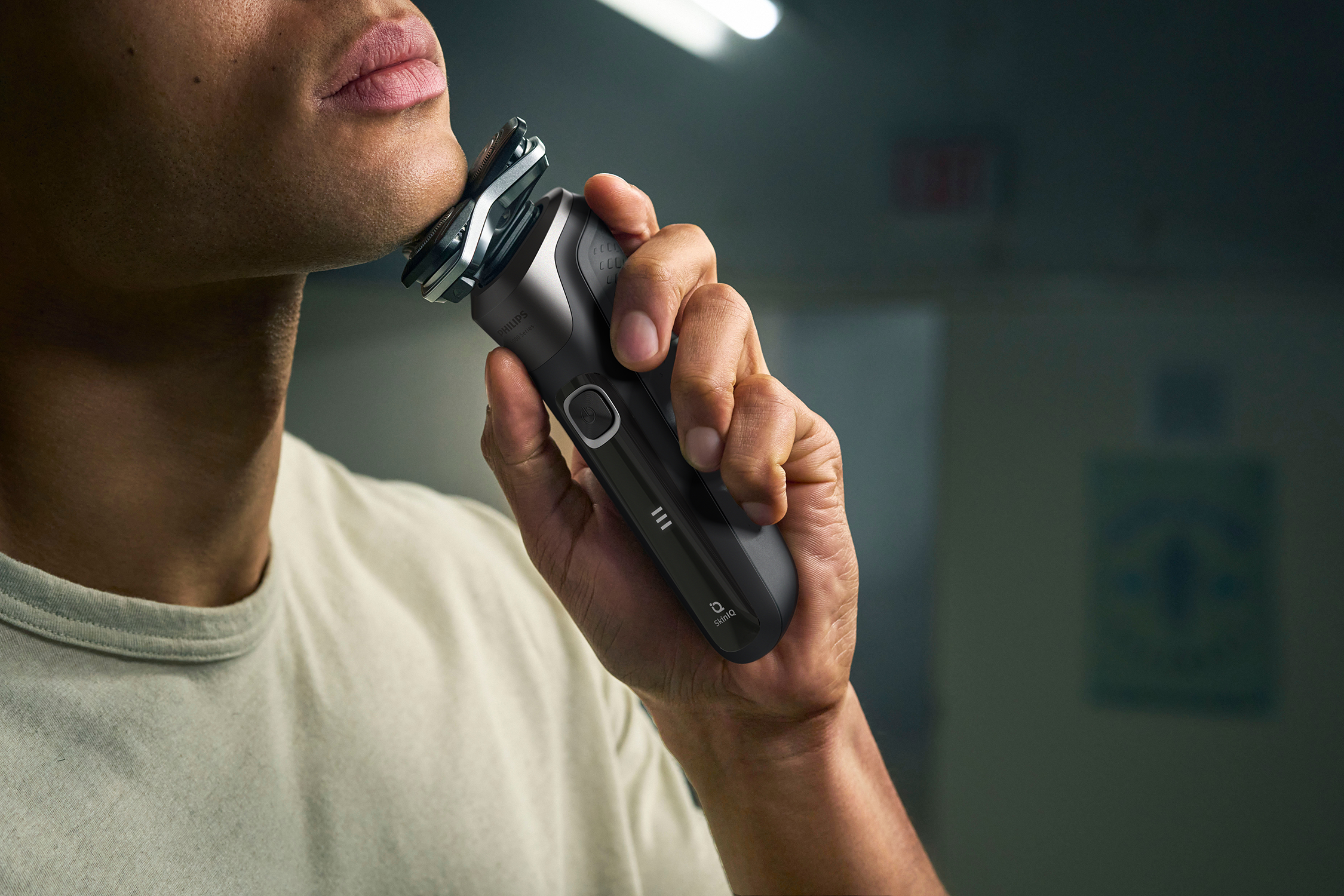 Man shaving his face with a black electric shaver, close-up, against a blurred background.
