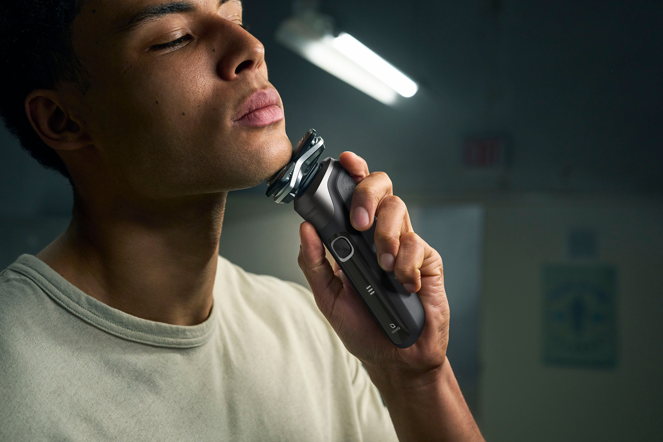 Man shaving his face with a black and silver razor. The background is blurred.