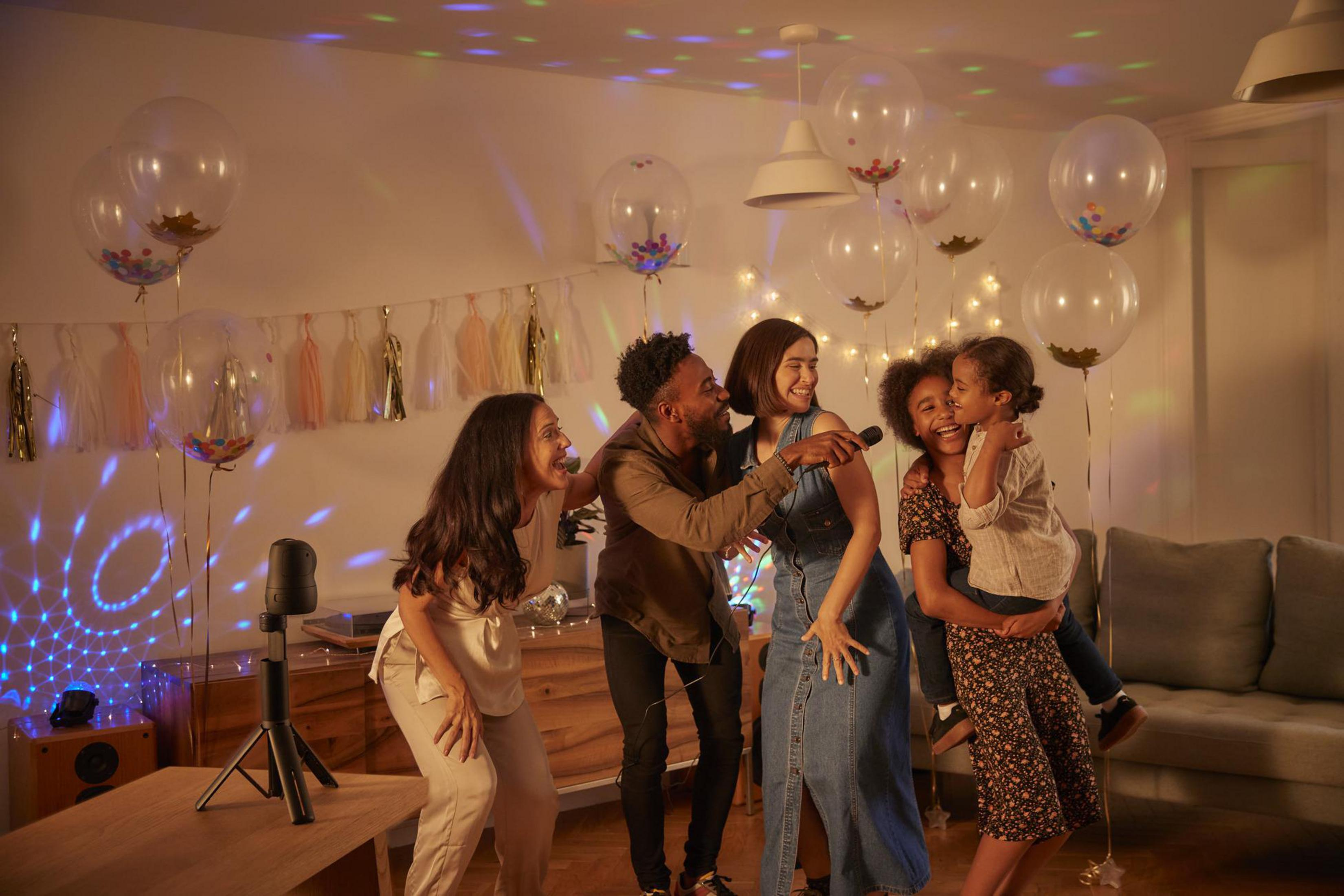 Gruppe von Leuten singt Karaoke in einem dekorierten Raum mit Luftballons.