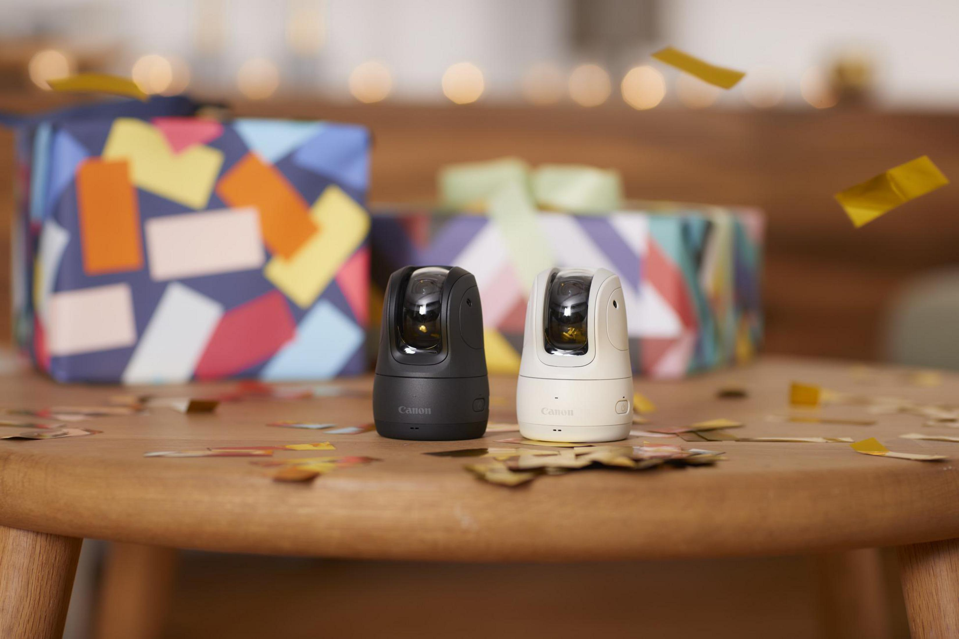 Zwei schwarz-weiße Kameras, umgeben von Konfetti und Geschenkboxen im Hintergrund.