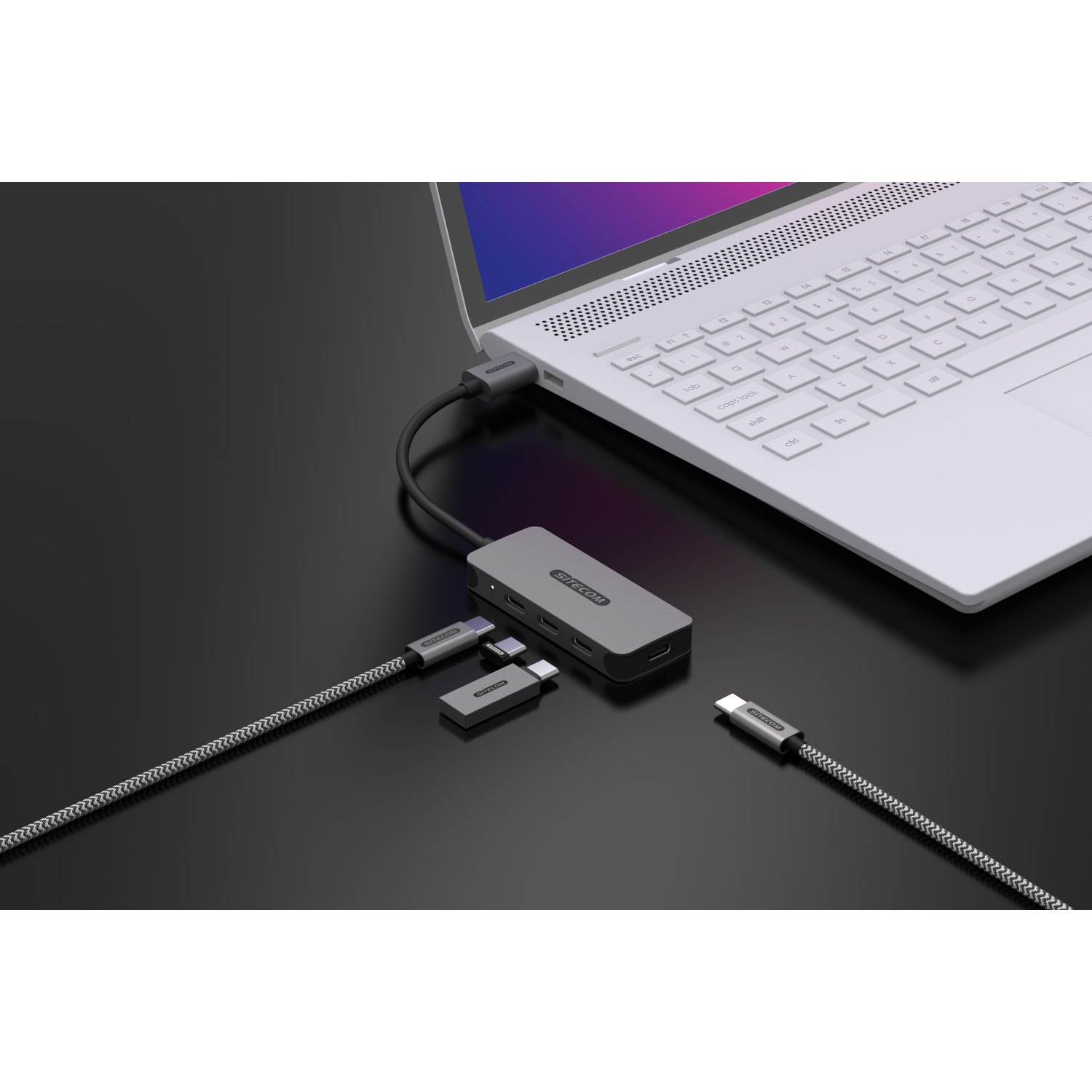Laptop con hub e diversi cavi collegati, tutto su superficie nera.