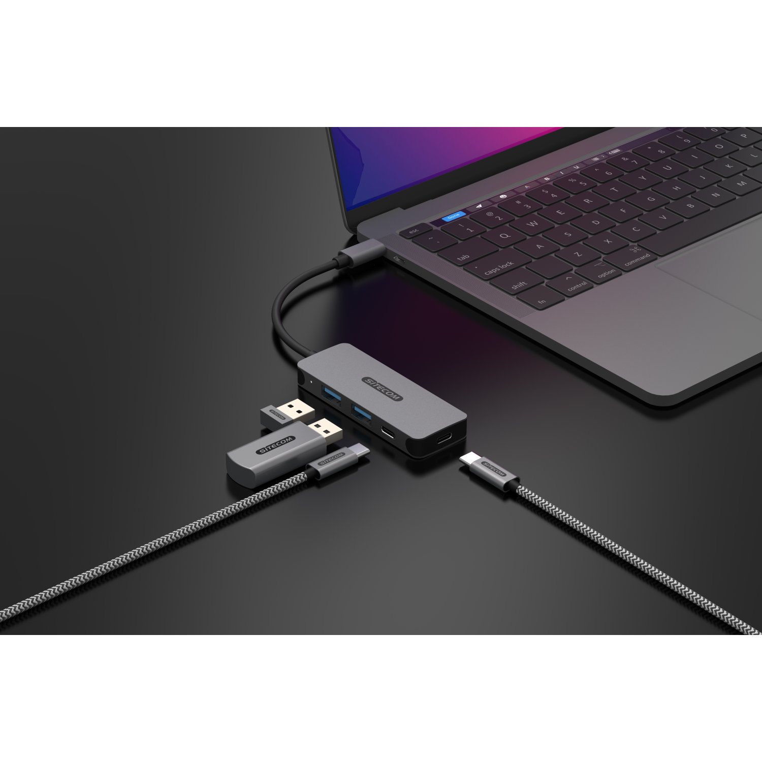 Laptop and several connected devices: USB hub, USB cables. All are on a dark surface.