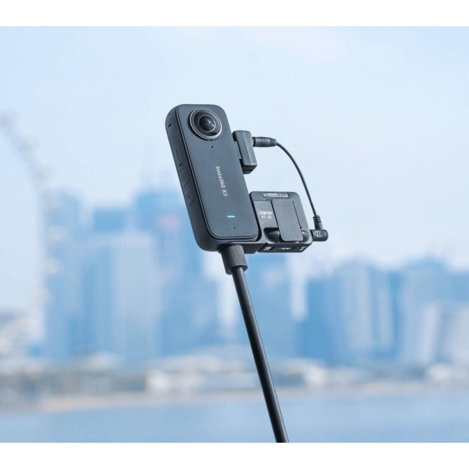 Una fotocamera nera su un bastone, con un microfono collegato. Lo sfondo è una città.