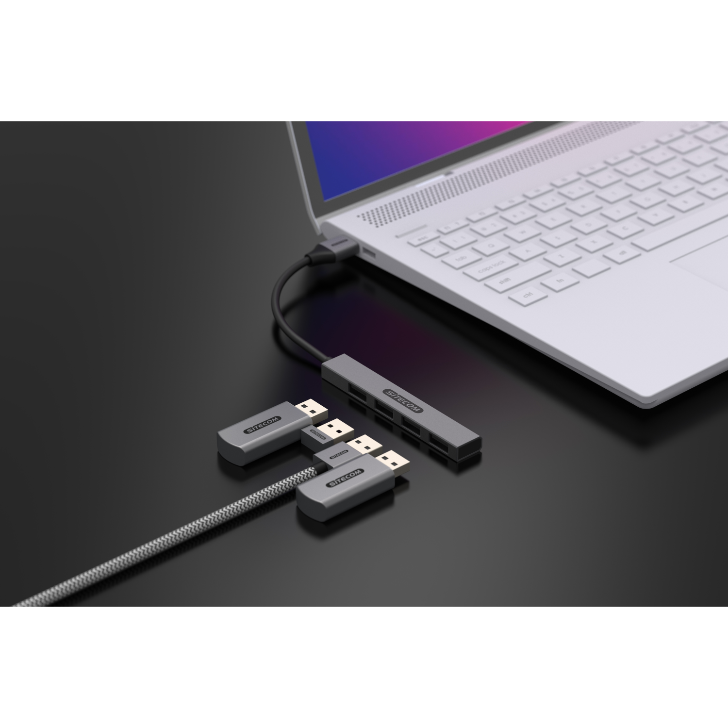 Tre adattatori SITECOM grigi collegati a un laptop su una superficie nera.