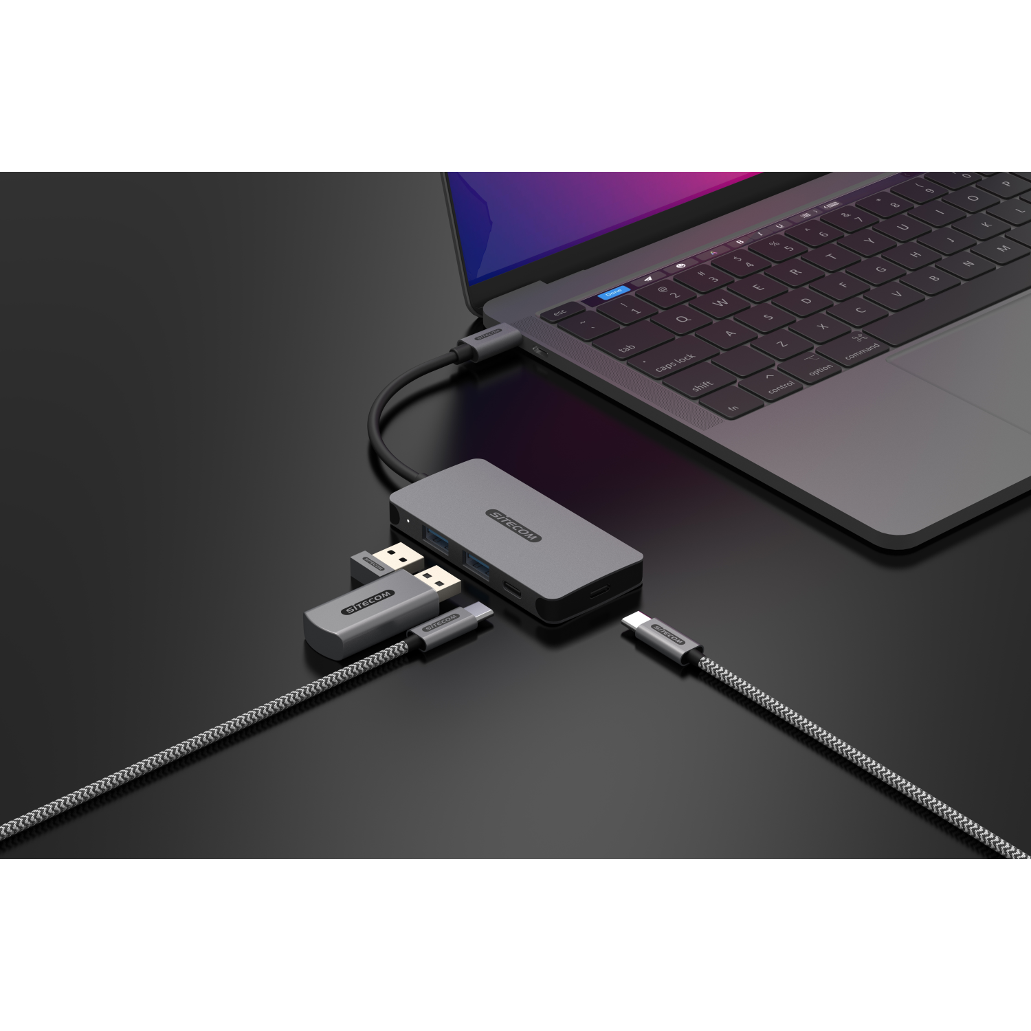 Laptop collegato a un hub Sitecom grigio con unità USB e cavi su una superficie scura.